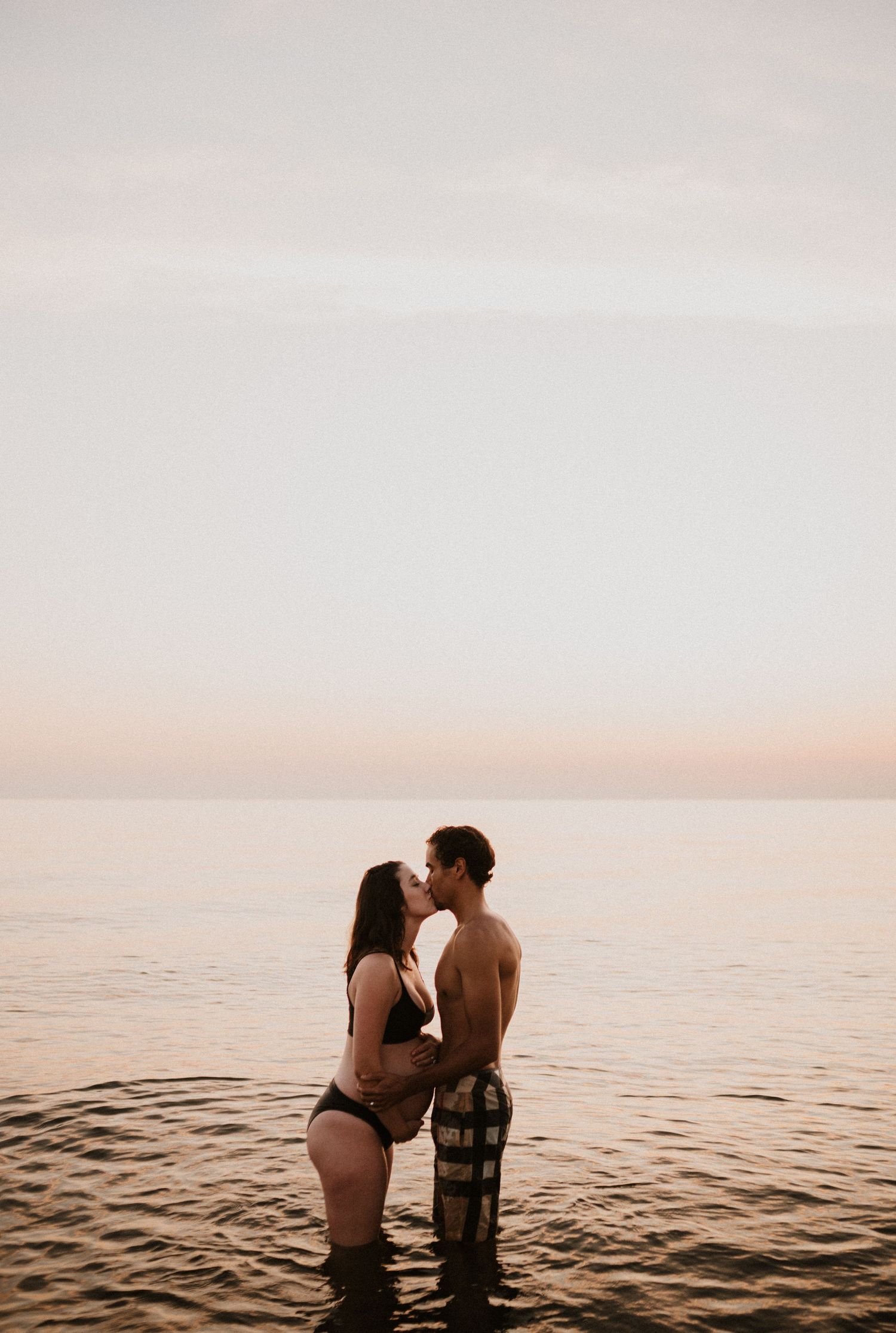 Couple sharing intimate moment while standing in ocean water at sunset.