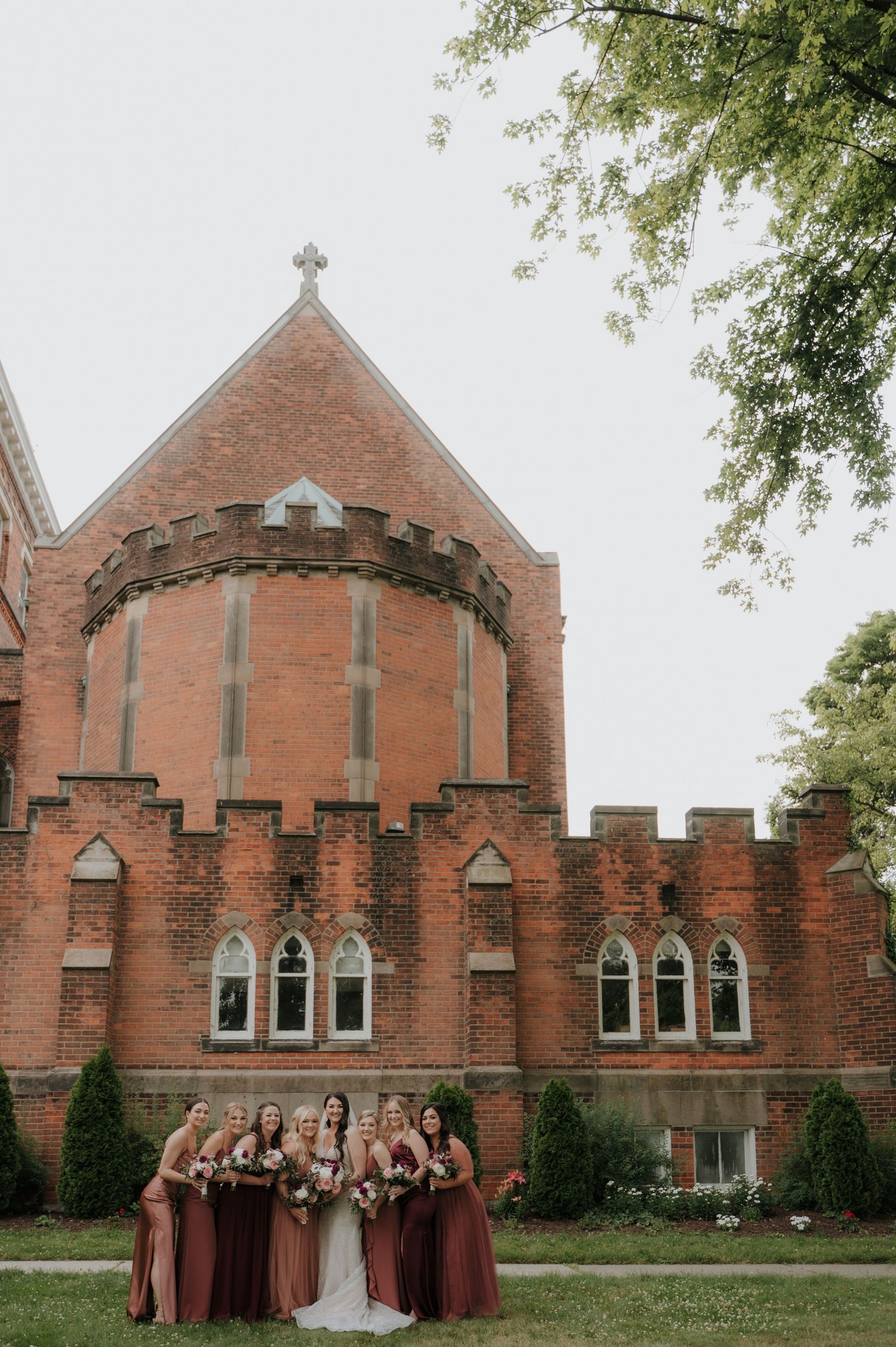 Gothic brick church exterior with wedding party in burgundy dresses.