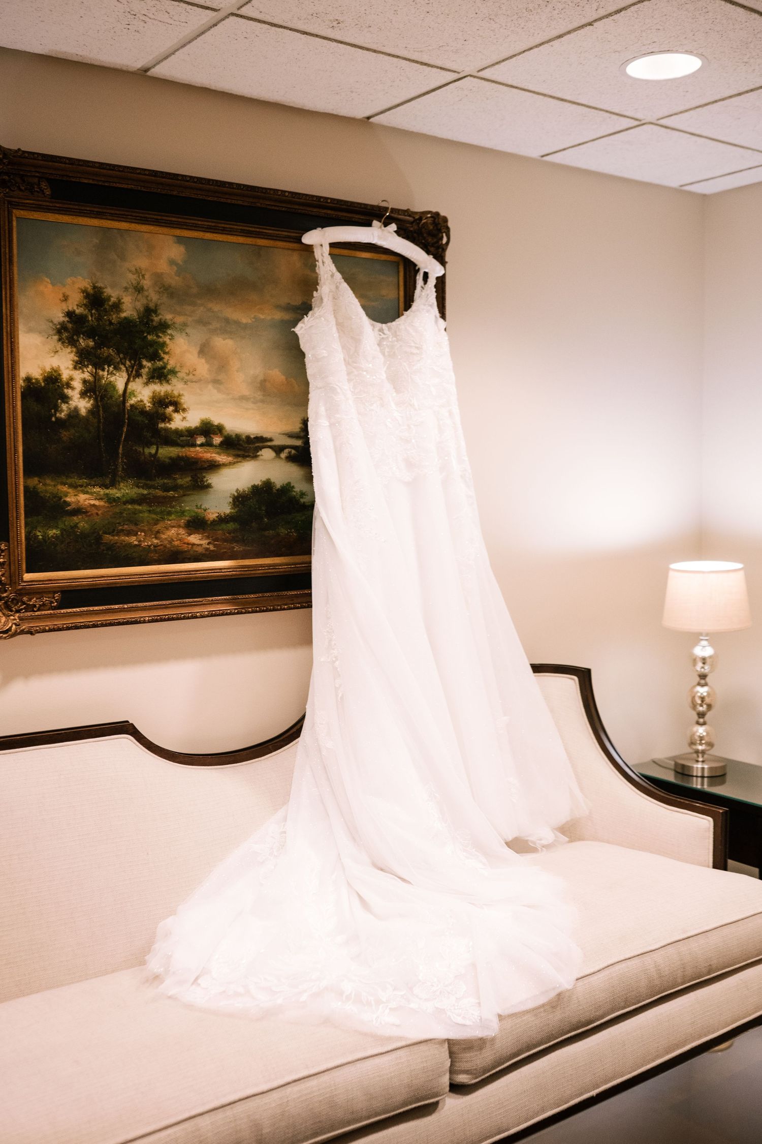 White wedding dress displayed on a couch with landscape paintings on the wall.