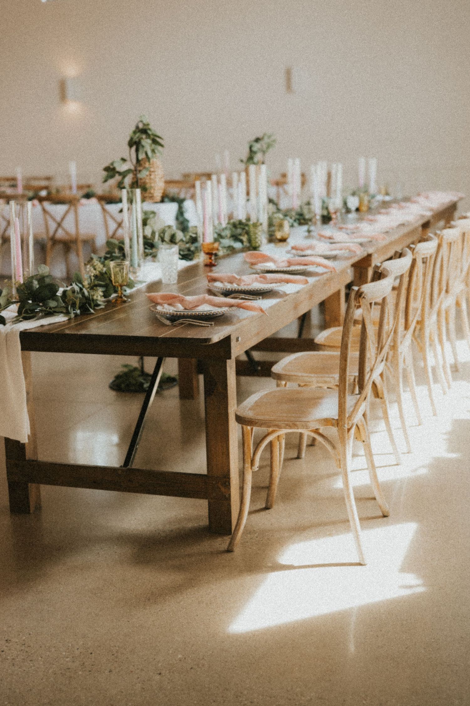 Minimalist wedding reception setup with long wooden tables and white chairs in natural light.