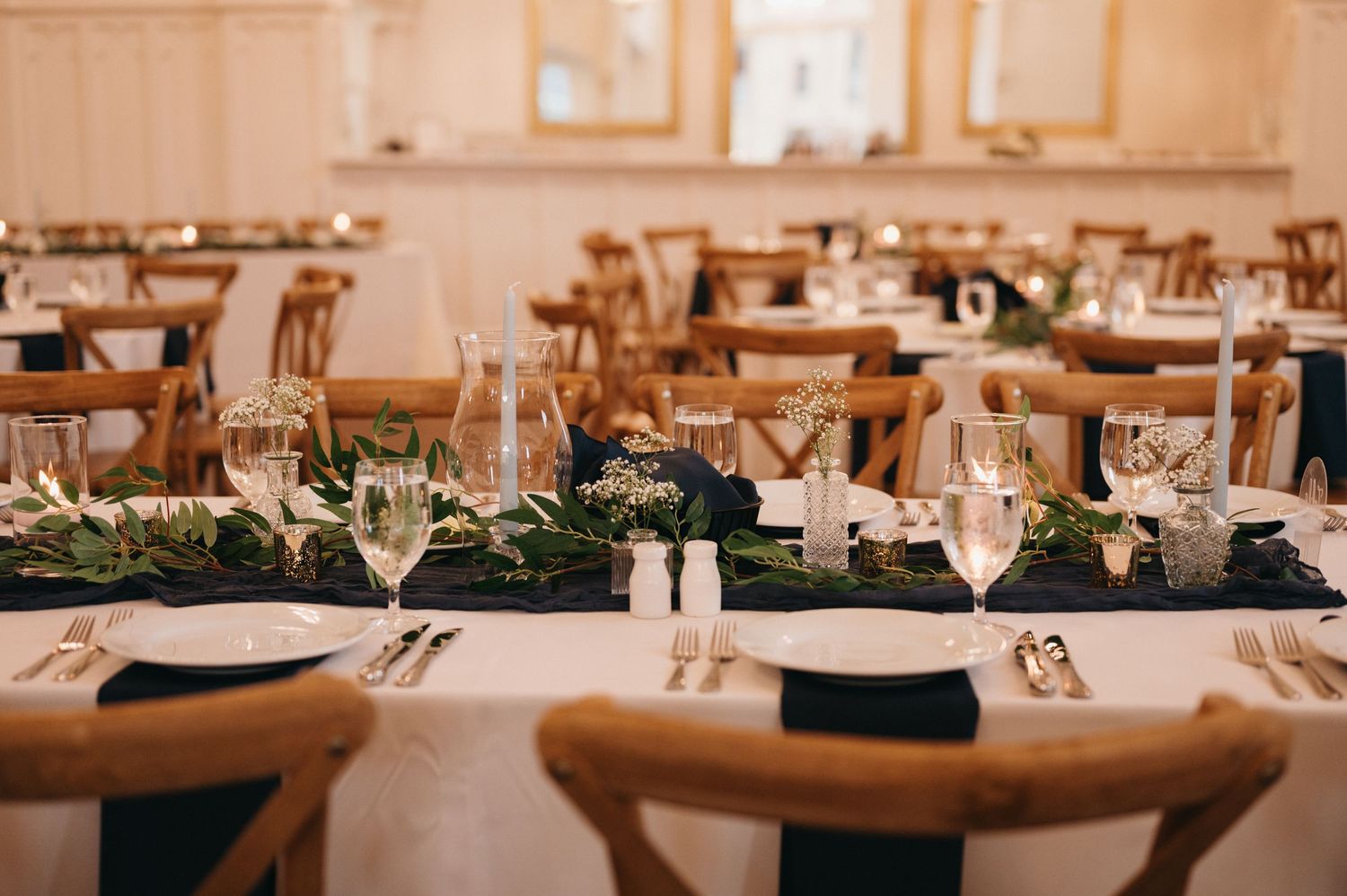 Elegant wedding reception table setting with greenery centerpieces and wine glasses.