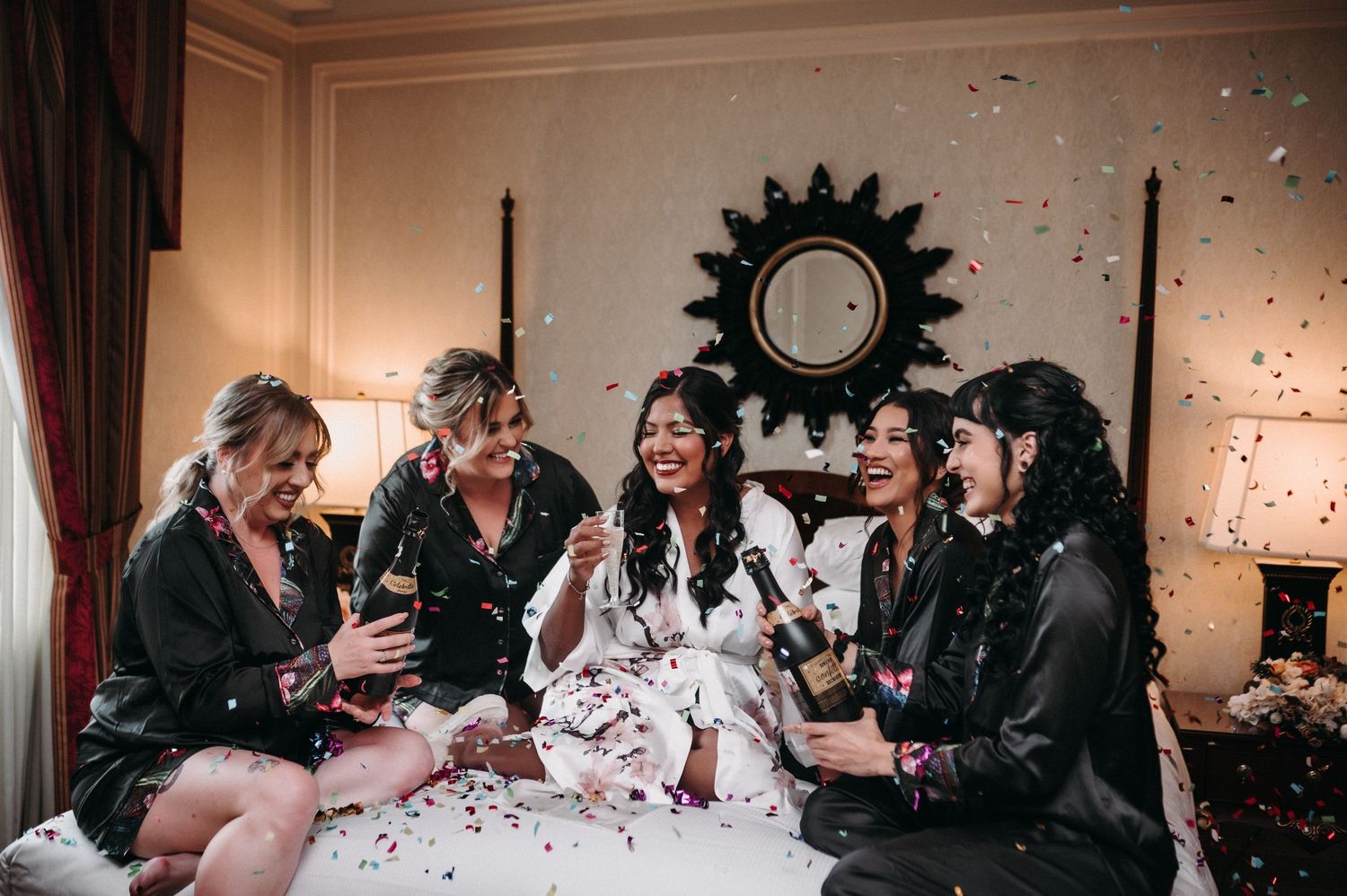 Celebratory scene with friends laughing amid confetti in elegant room with sunburst wall decor.