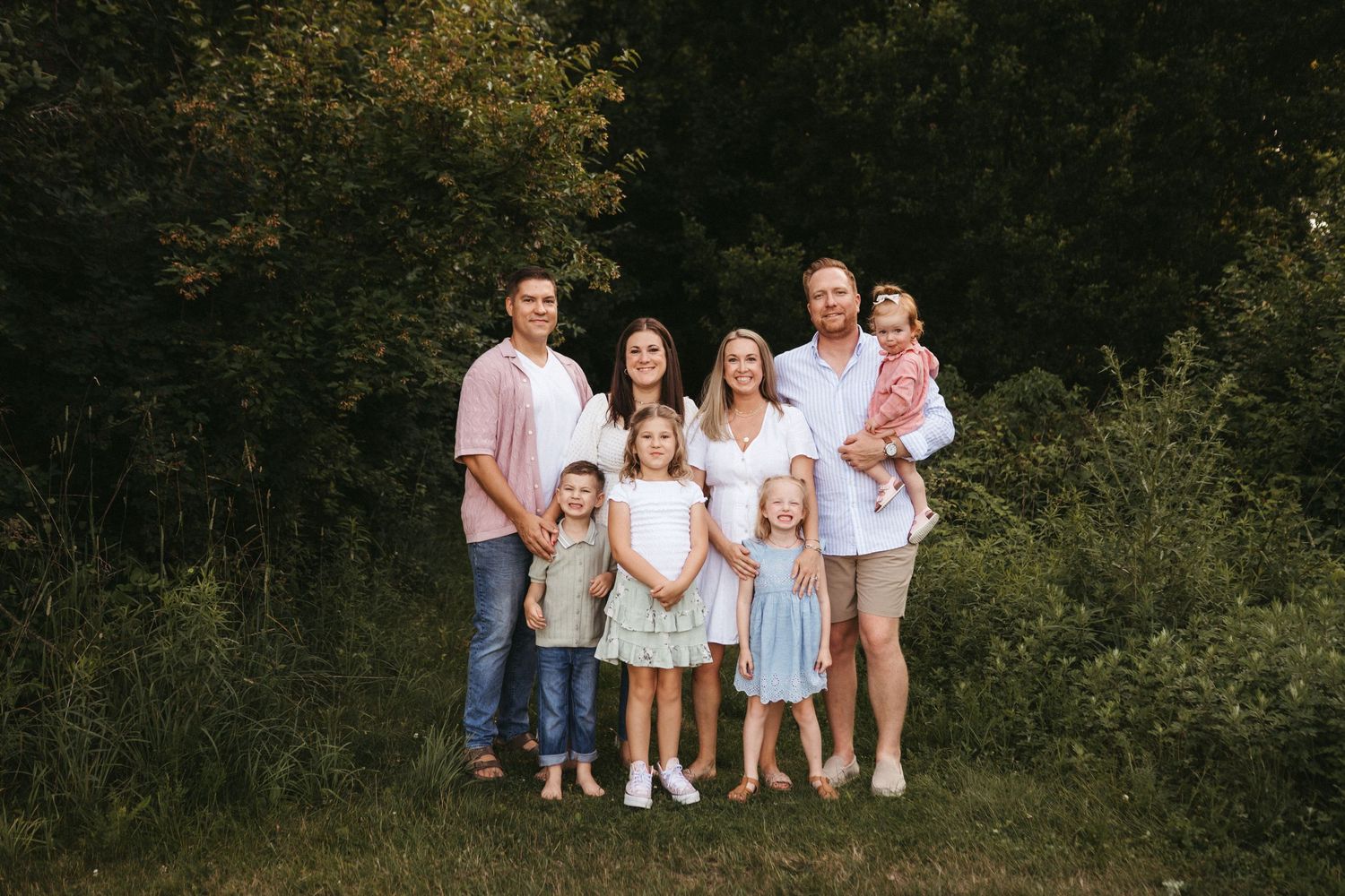 Multi-generational family portrait outdoors with everyone wearing coordinated light-colored outfits.
