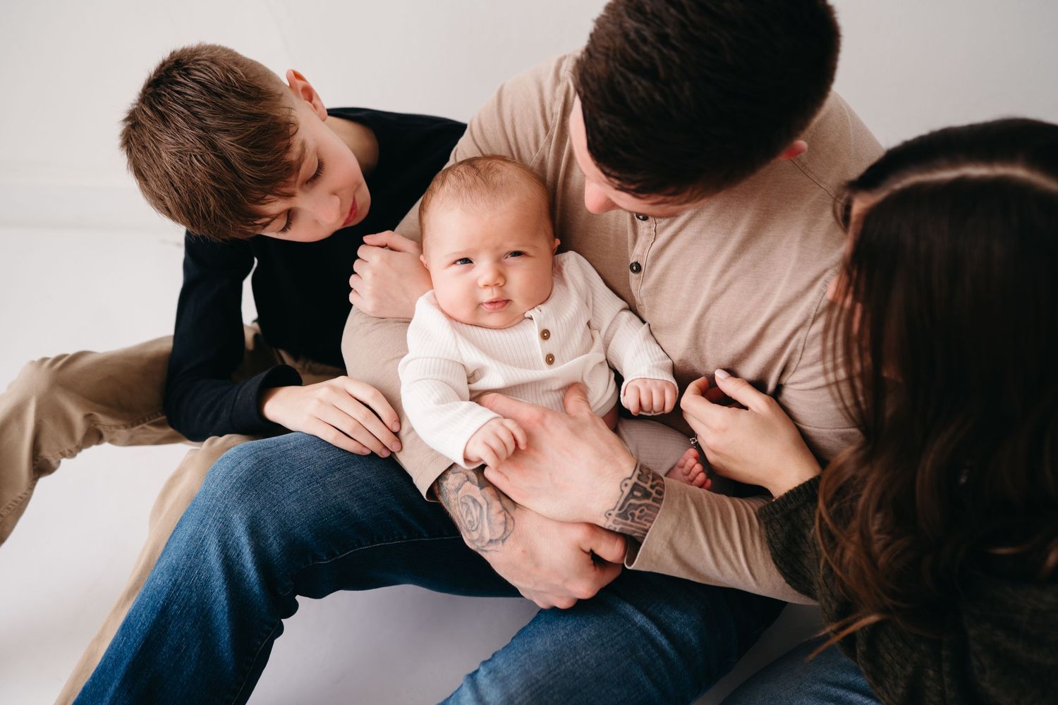 Family snuggling together with baby on floor against white background.