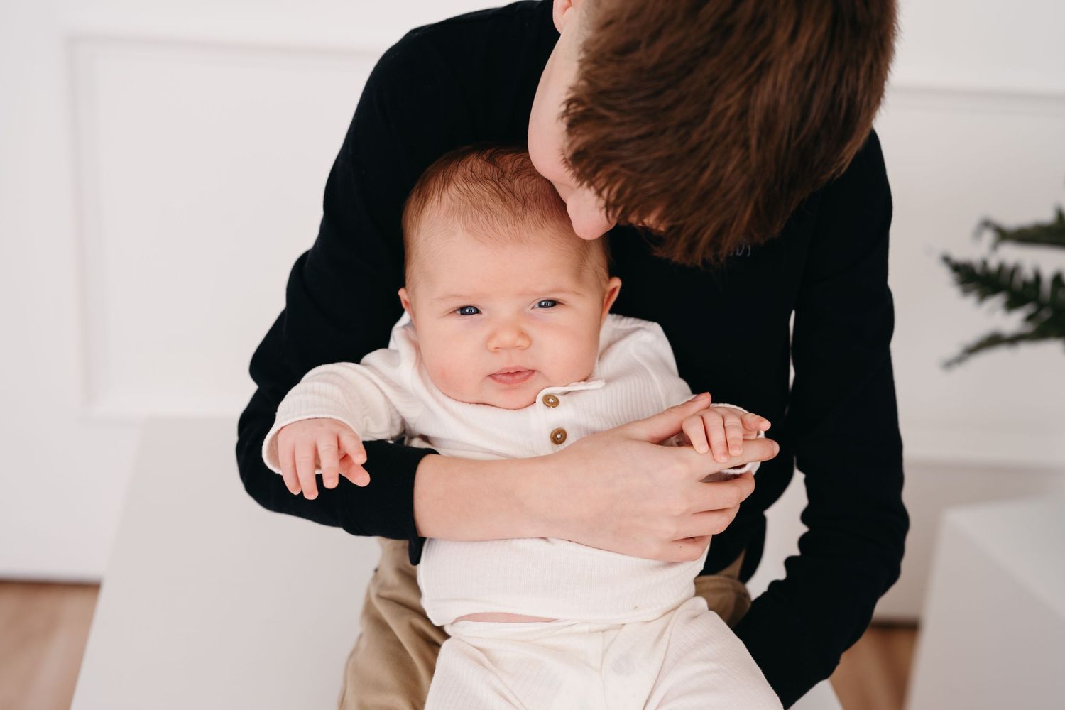A baby in white clothing is being held and supported while looking directly at the camera.
