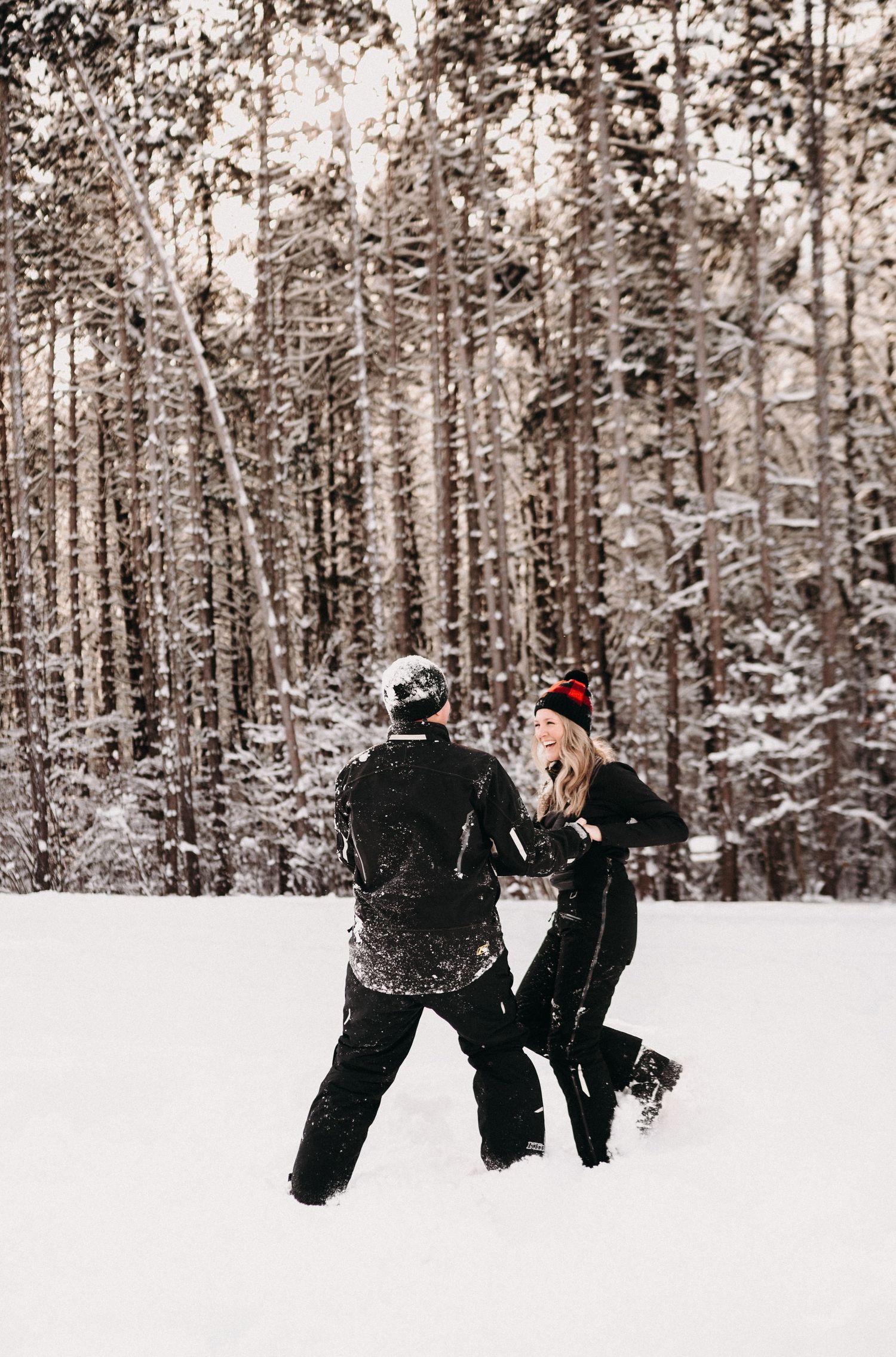 Two people in winter gear walking through deep snow in a forest setting.