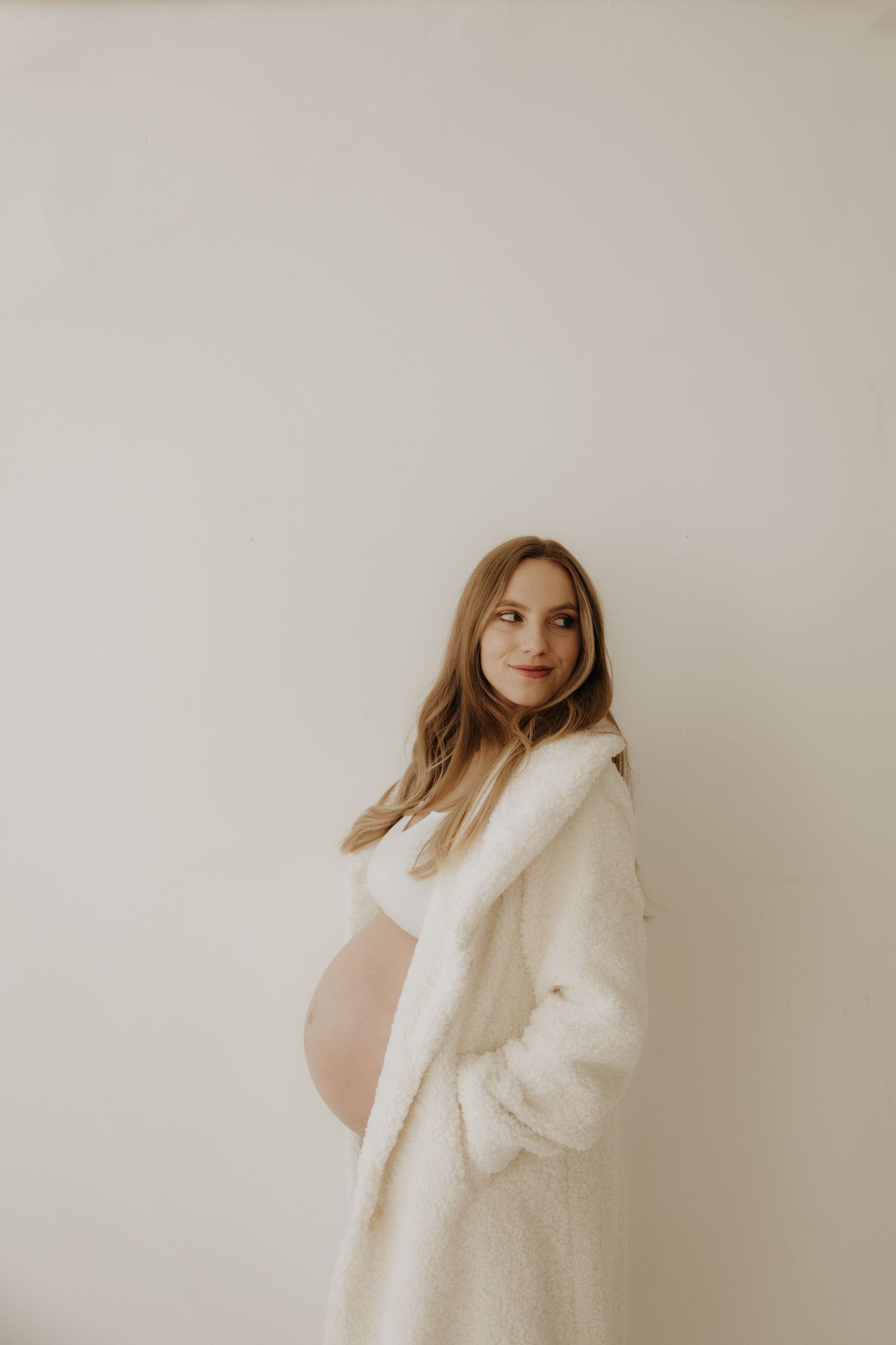 Maternity portrait featuring a cozy white teddy coat against minimal background.