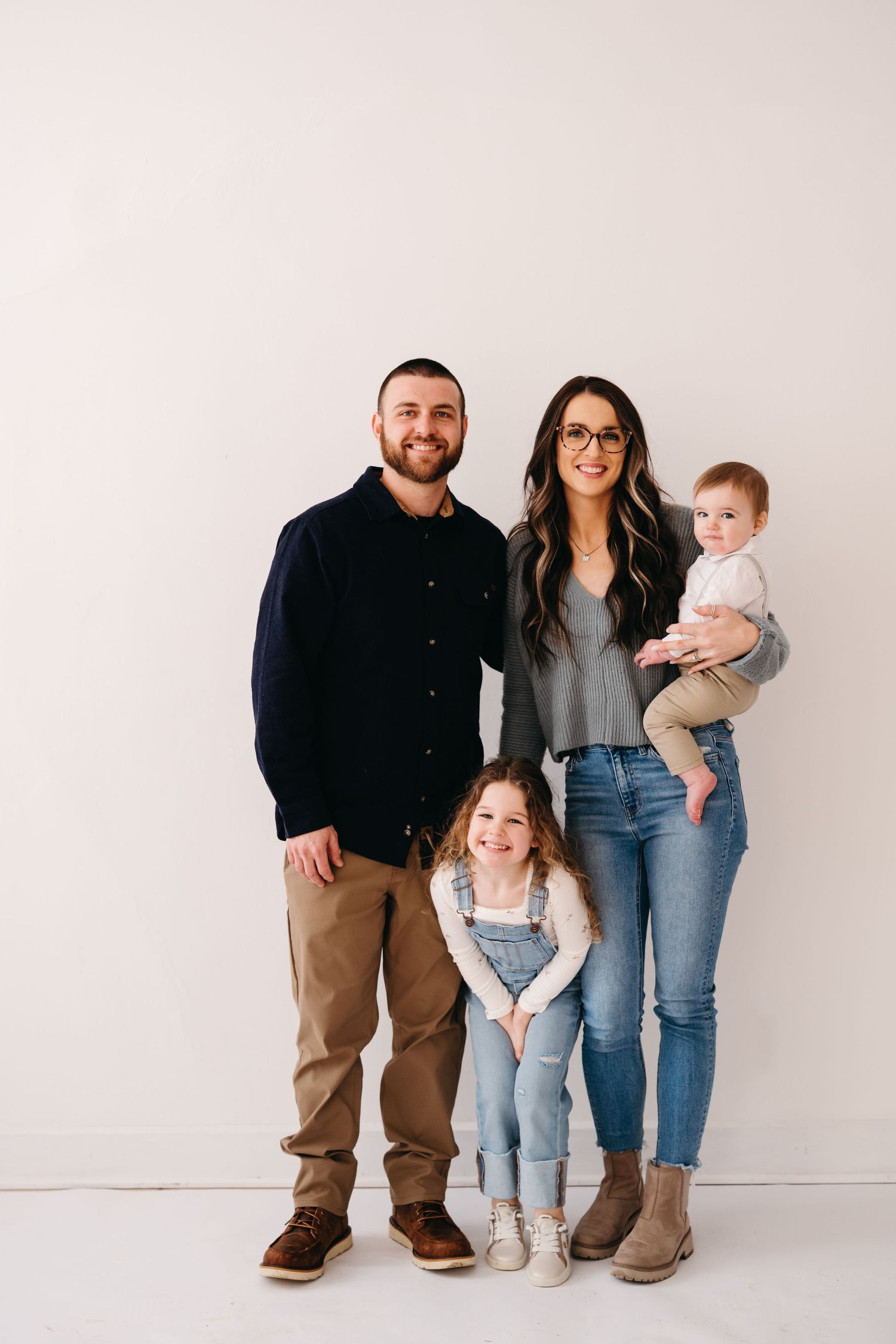A family wearing coordinated casual outfits poses together against a white wall.