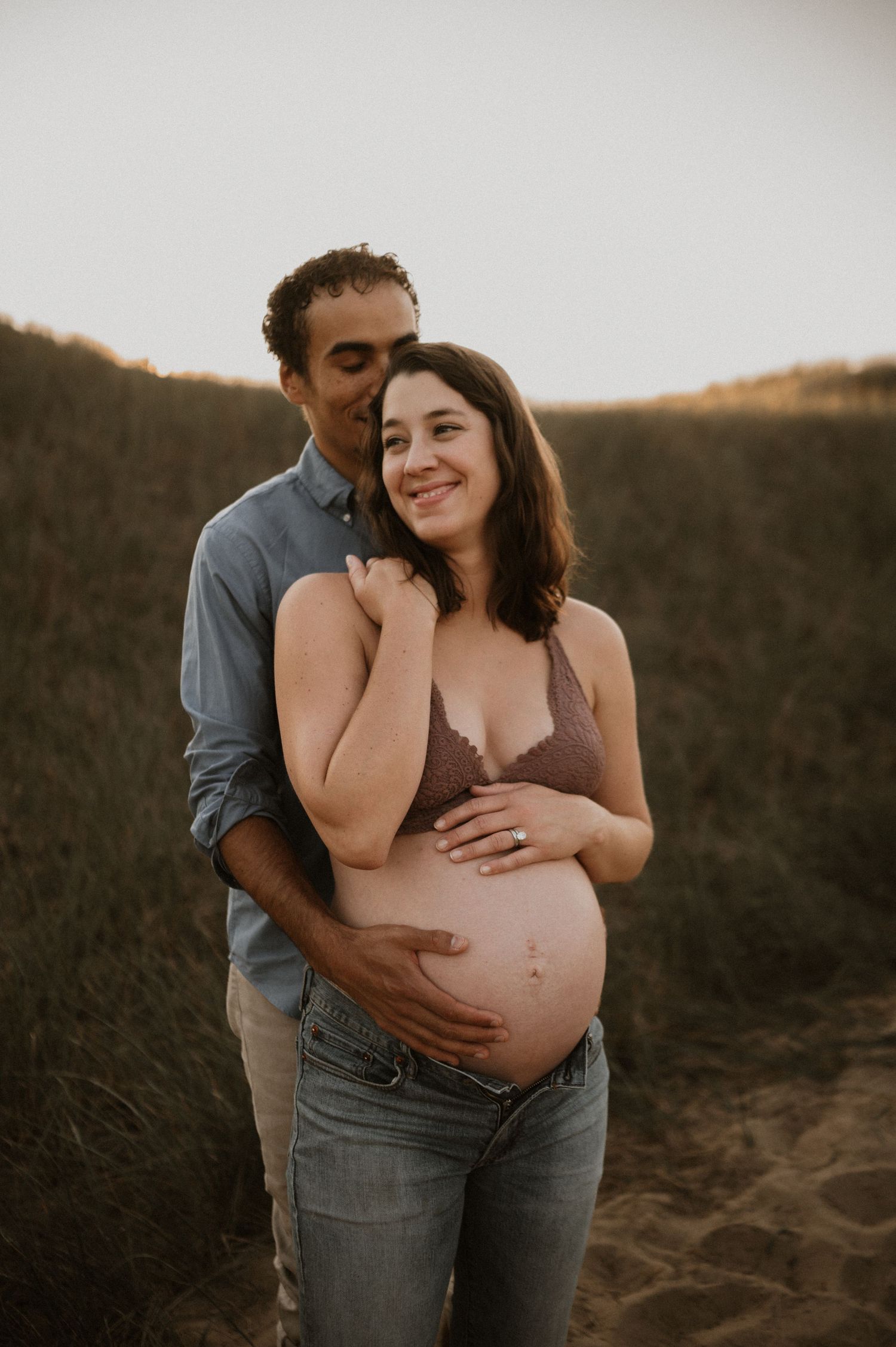 Romantic maternity portrait of couple sharing tender moment during sunset photoshoot.