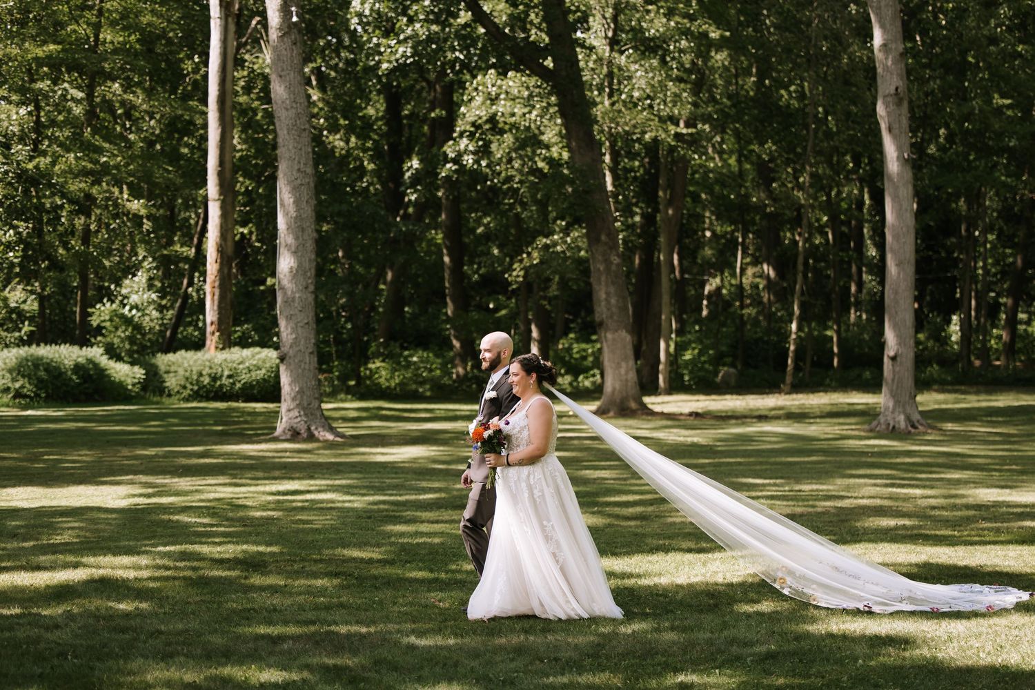 Wedding couple photographed from afar walking through a scenic wooded area.