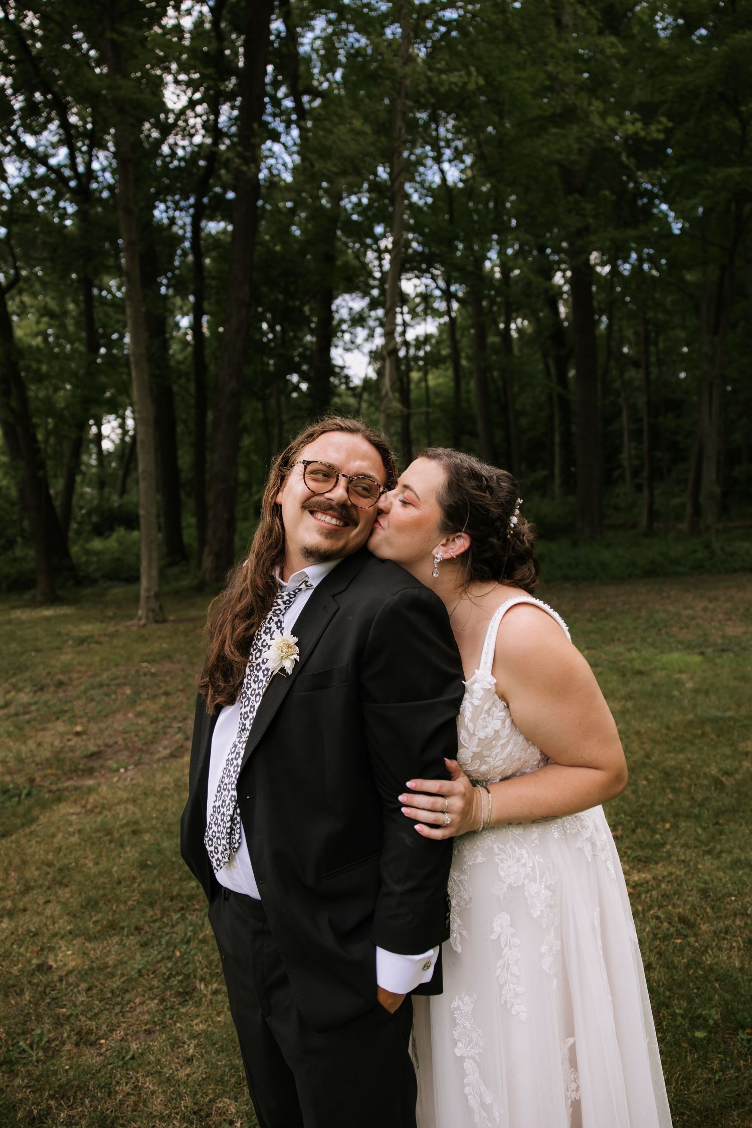 A couple laughs and embraces during their outdoor wedding photos in a wooded area.