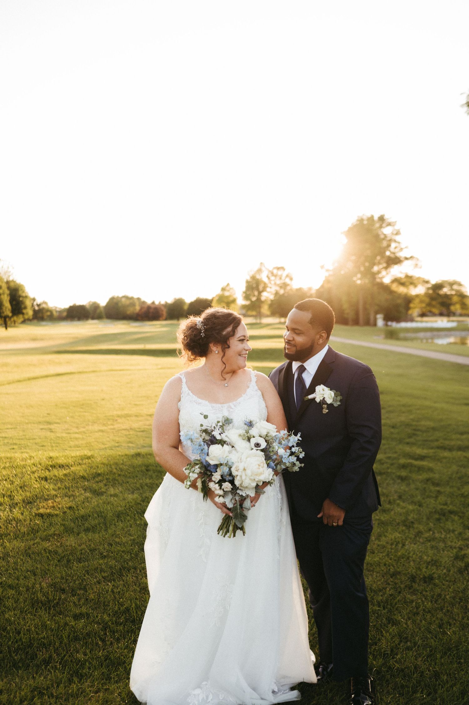 A couple shares an intimate moment in a sunlit field during their wedding photoshoot at golden hour.