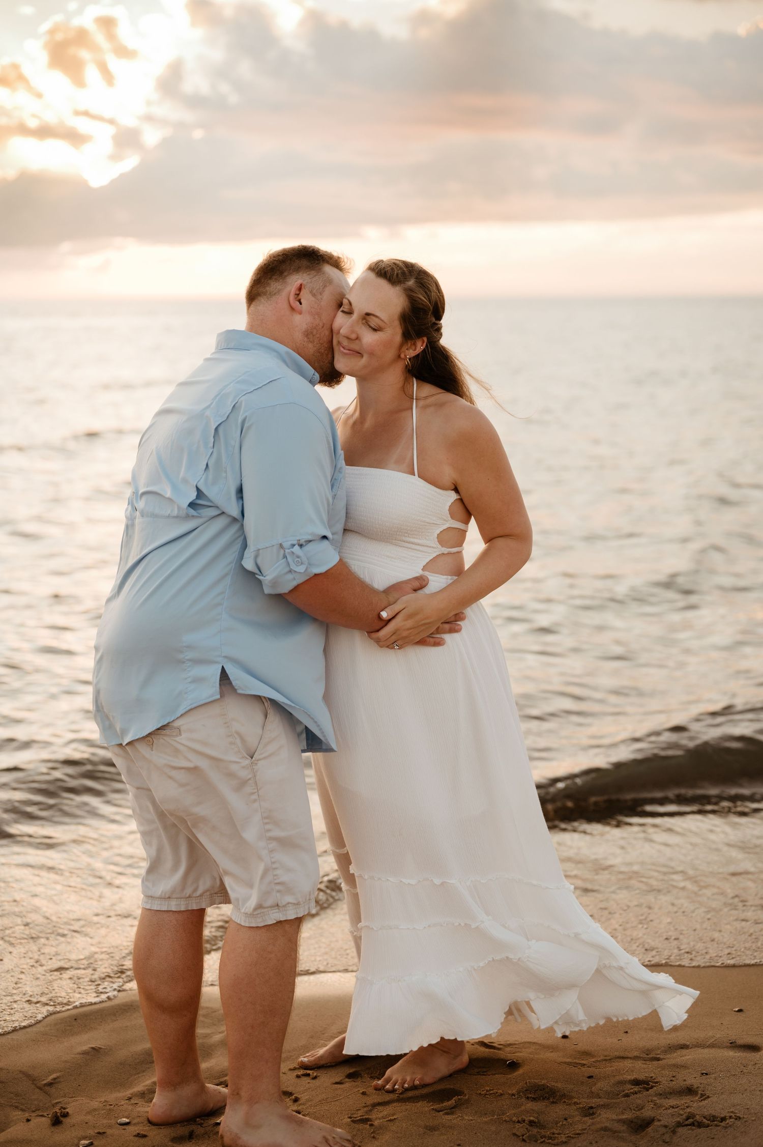 A romantic beach wedding photo at sunset with a couple embracing on the sandy shore near the ocean.