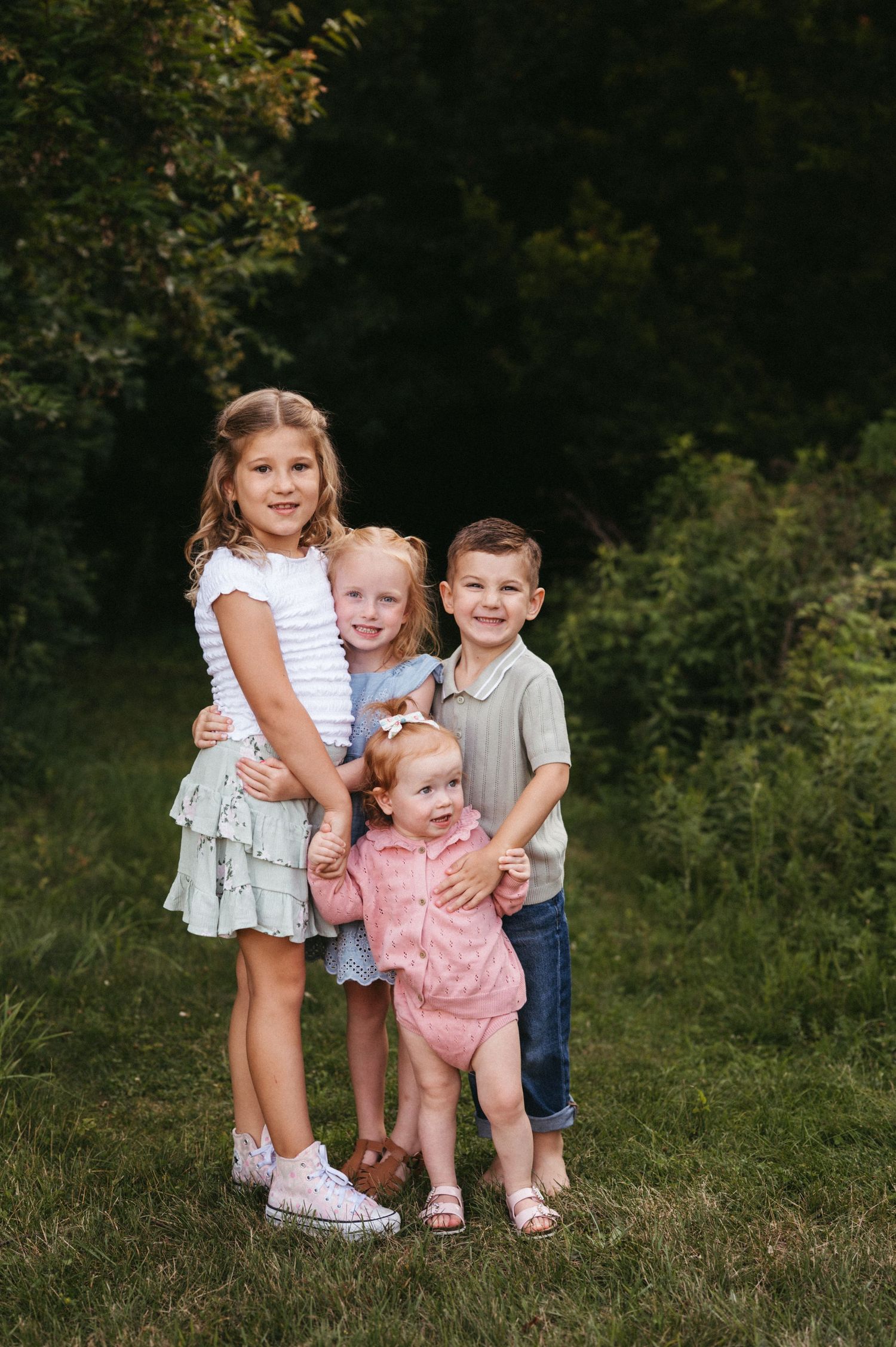 Group of children in coordinating outfits pose together on grass during summer photo session.