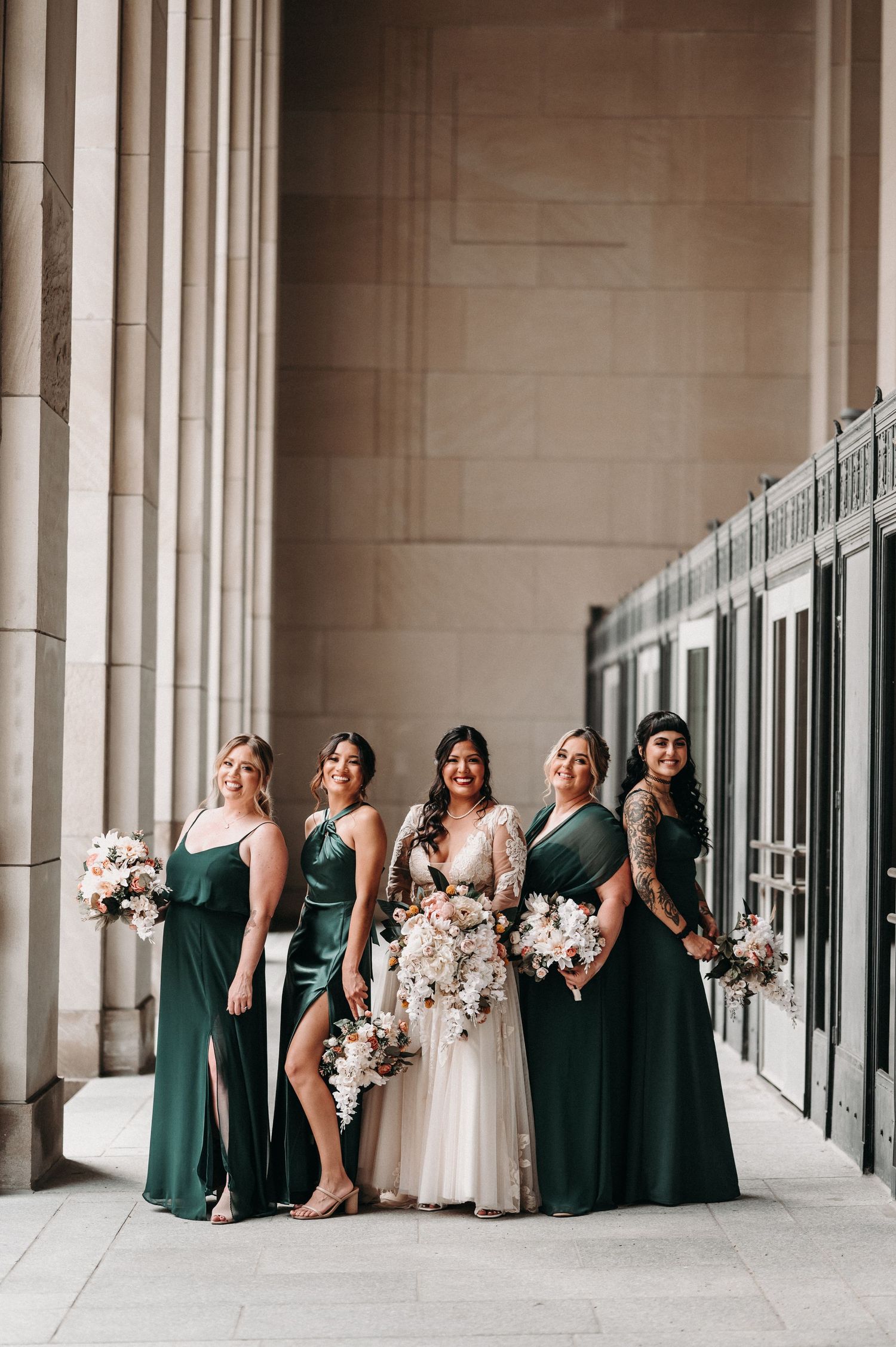 Wedding party in emerald green and white poses elegantly against stone columns.