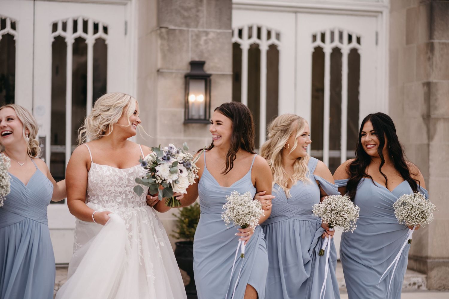 Bridesmaids in powder blue dresses carry bouquets while walking with bride.