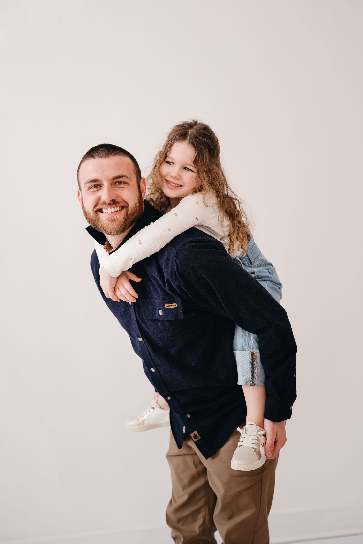 A joyful piggyback ride between parent and child wearing casual clothes against a light background.