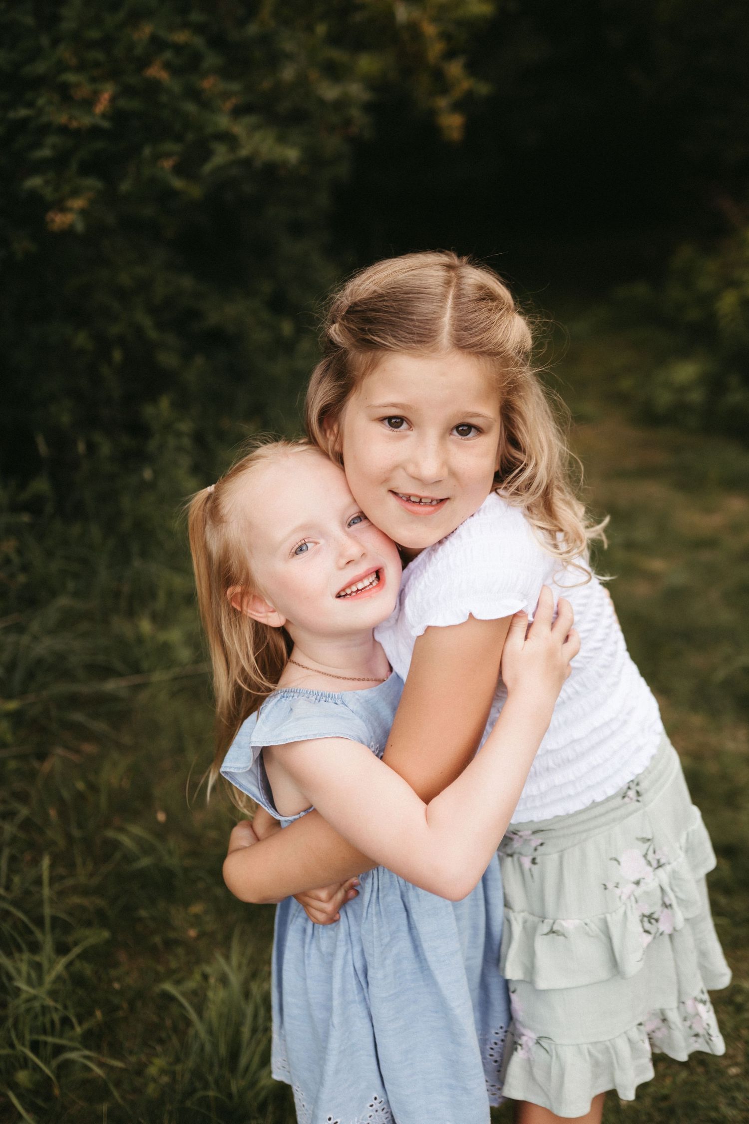 Sweet moment between children in blue and white dresses against a dark background.