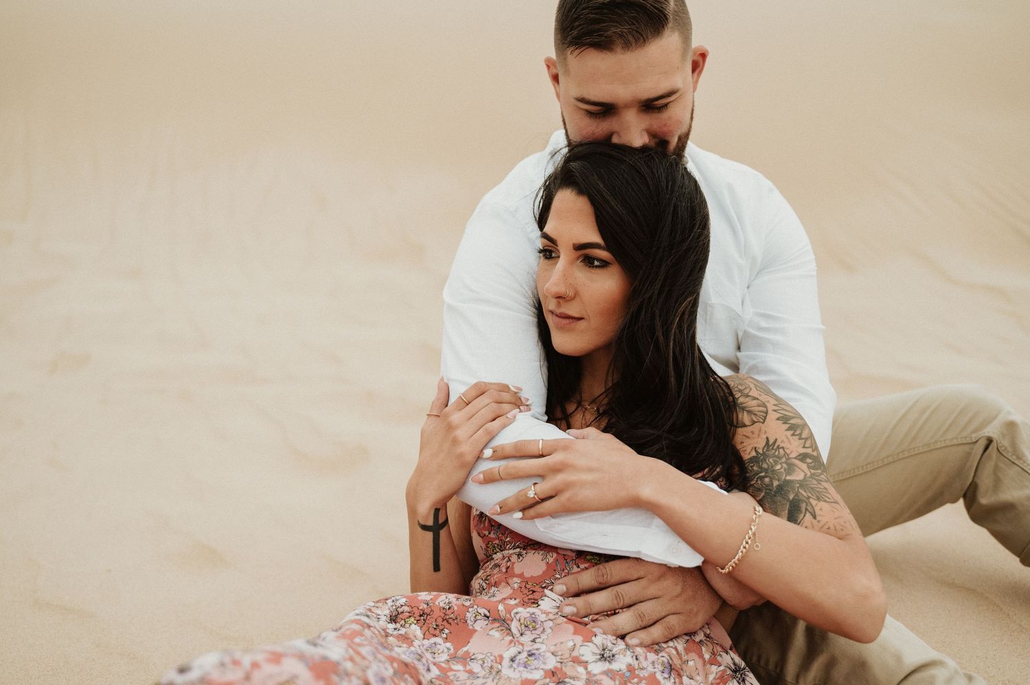 A couple shares an intimate moment while sitting on desert sand dunes.