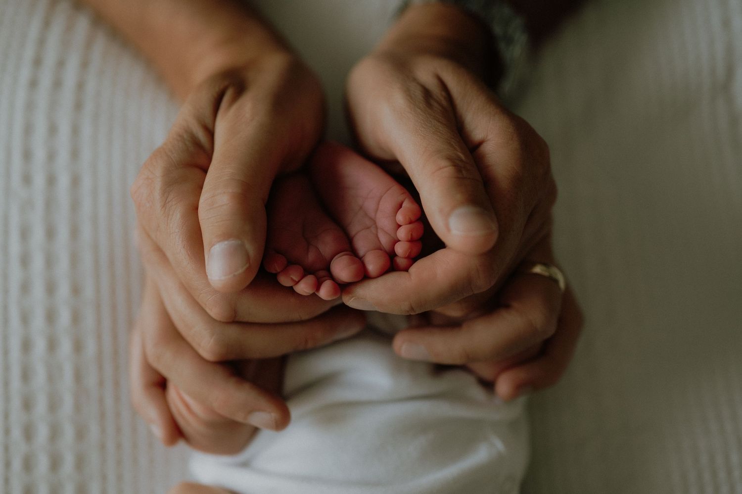 Close-up shot of hands gently intertwined against a neutral background.