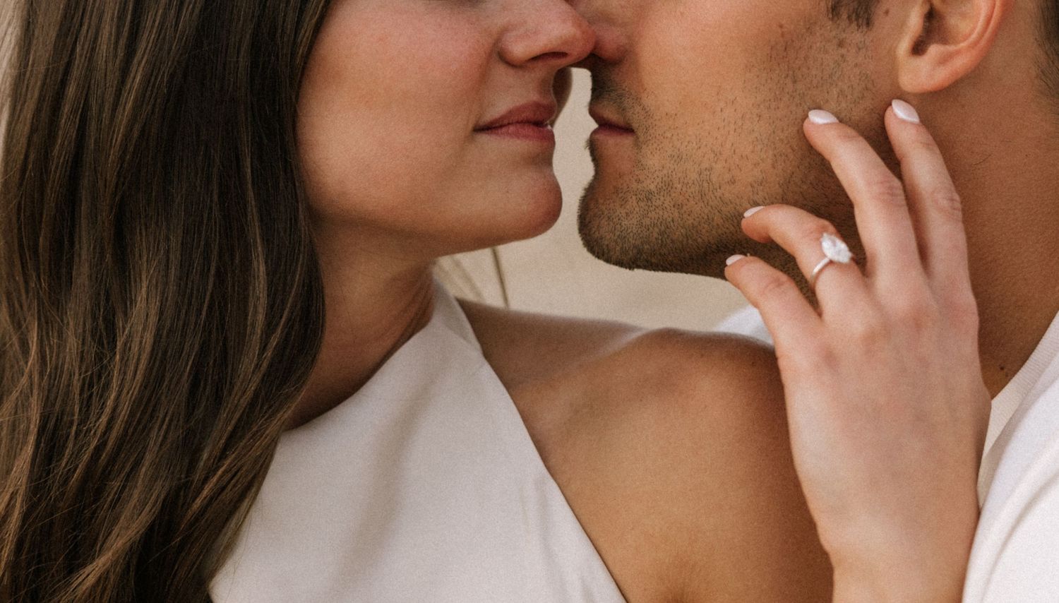 Close-up of a romantic couple sharing an intimate moment, woman wearing an engagement ring touching man's face.