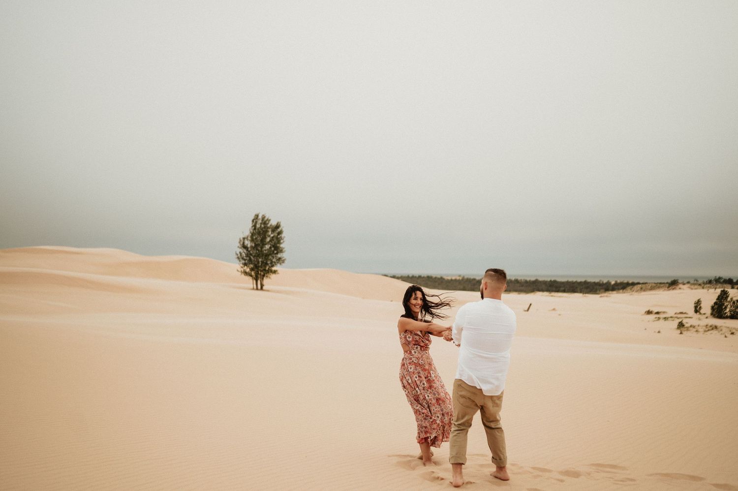 A romantic dance between two people on desert sand dunes with sparse vegetation in the background.