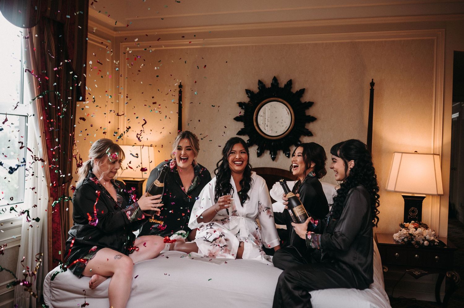 Group celebration with confetti in elegant room with sunburst mirror and table lamps.