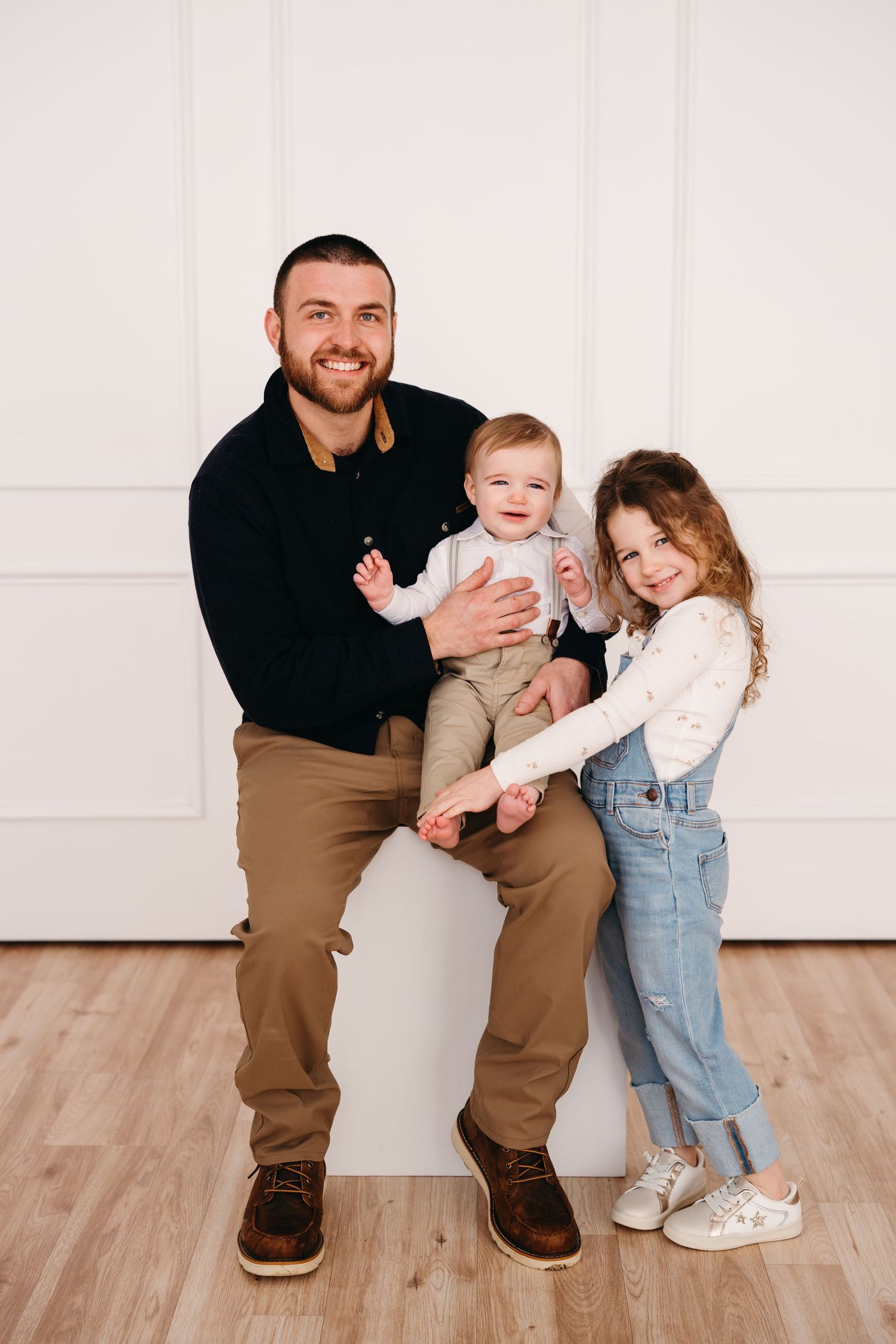 Family portrait against white wall with hardwood floors in casual attire.