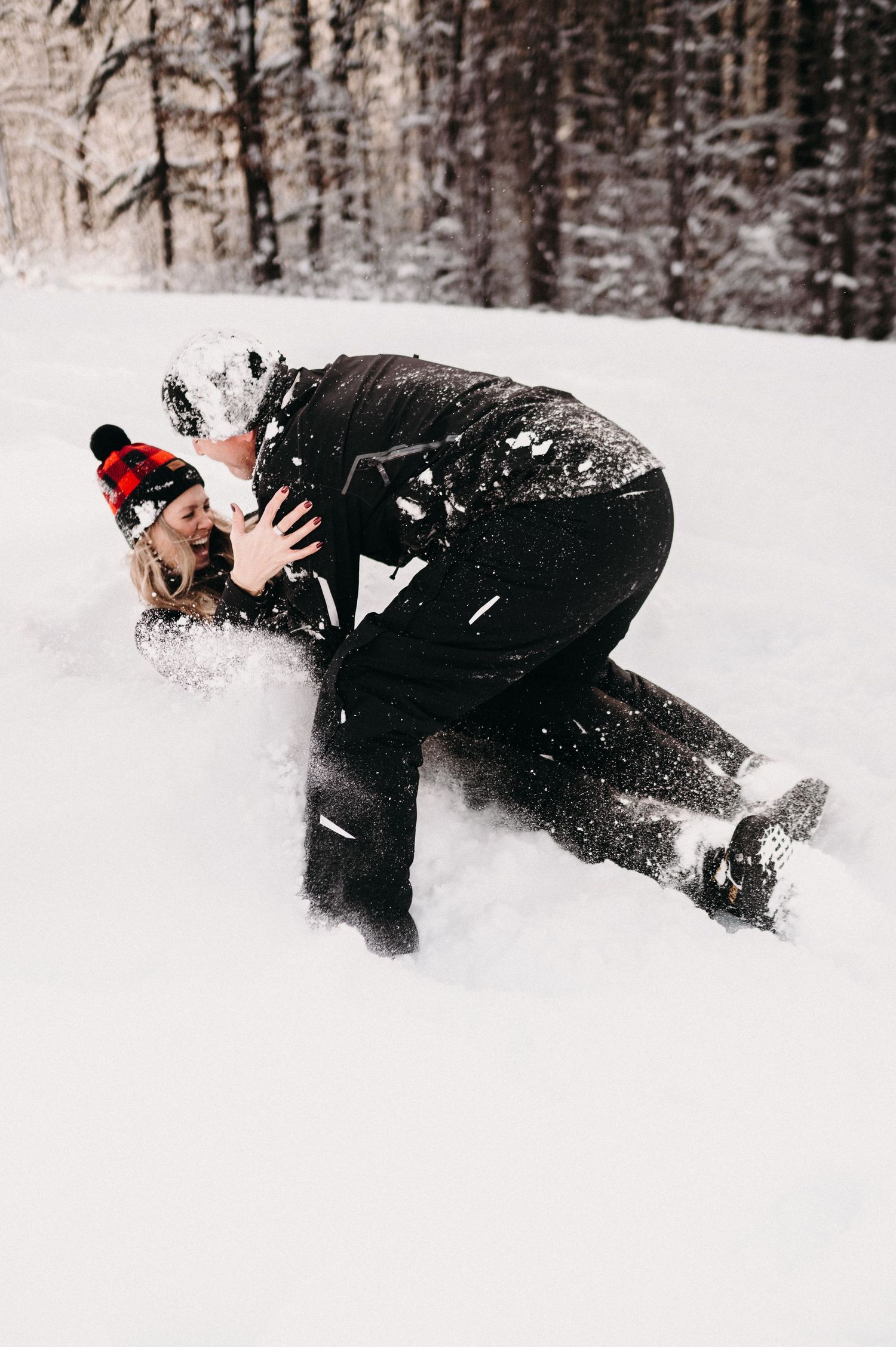 Person falling backwards into deep snow while wearing winter clothing and a red pom beanie.
