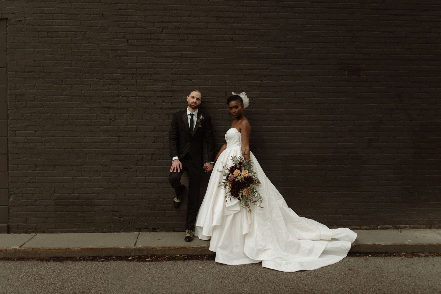 Artistic black and white wedding portraits against an industrial brick wall backdrop.