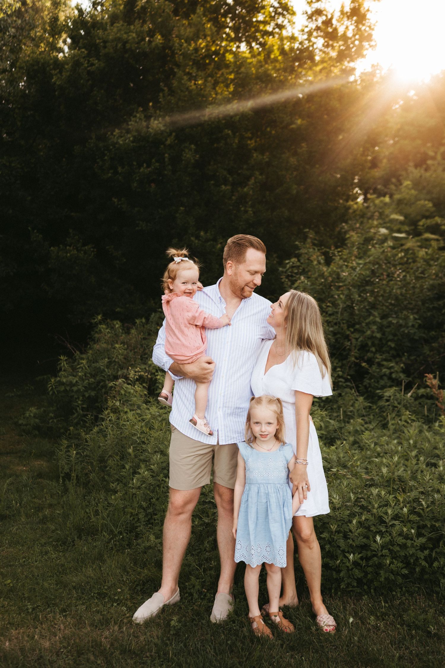 A family poses together in a garden at sunset wearing coordinated light colored outfits.