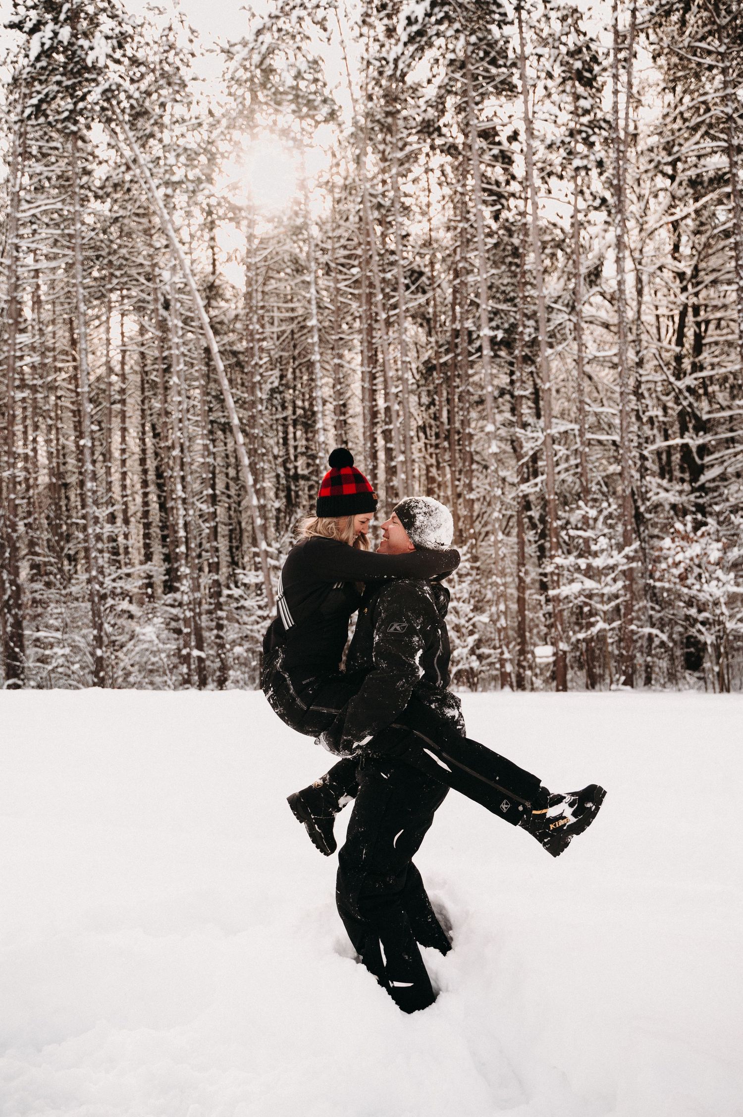 Silhouette of couple embracing in snowy forest with sunlight filtering through trees.
