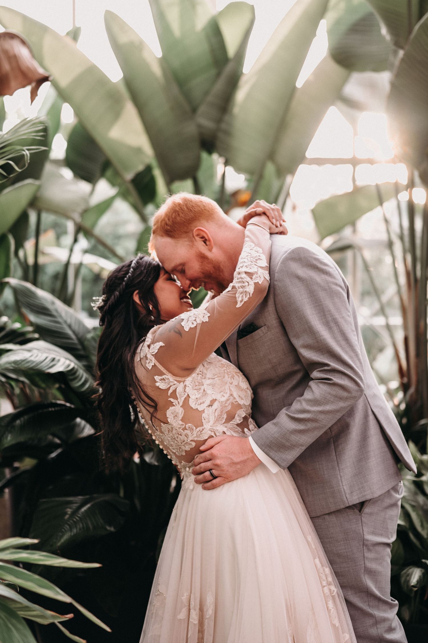 Romantic wedding portrait with couple embracing among large tropical leaves.