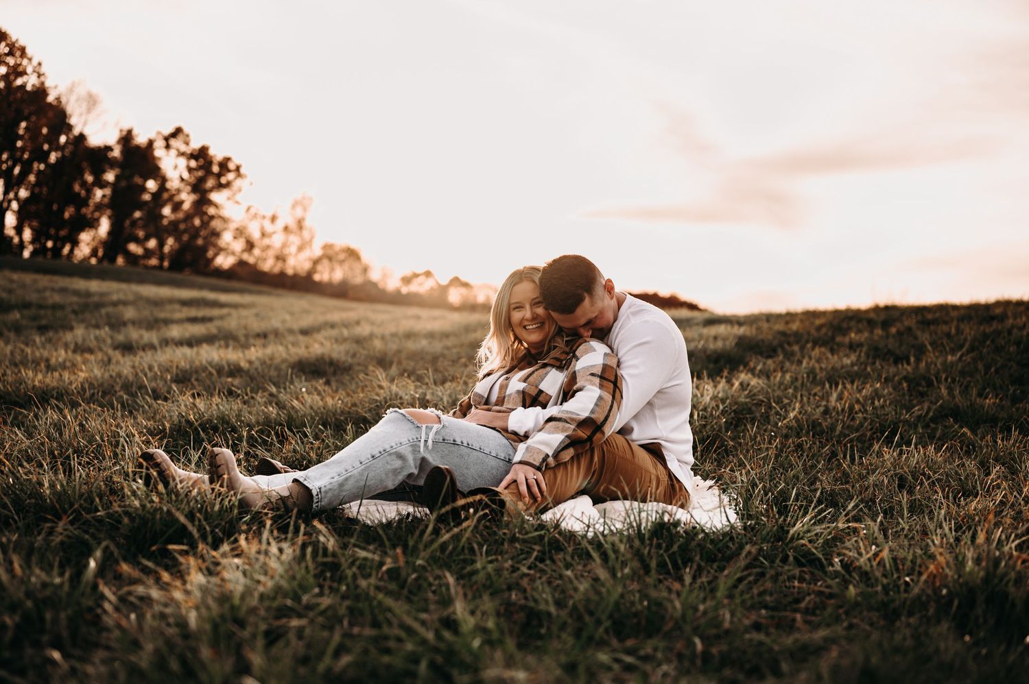 Couple relaxing together on grassy hillside during golden hour sunset.
