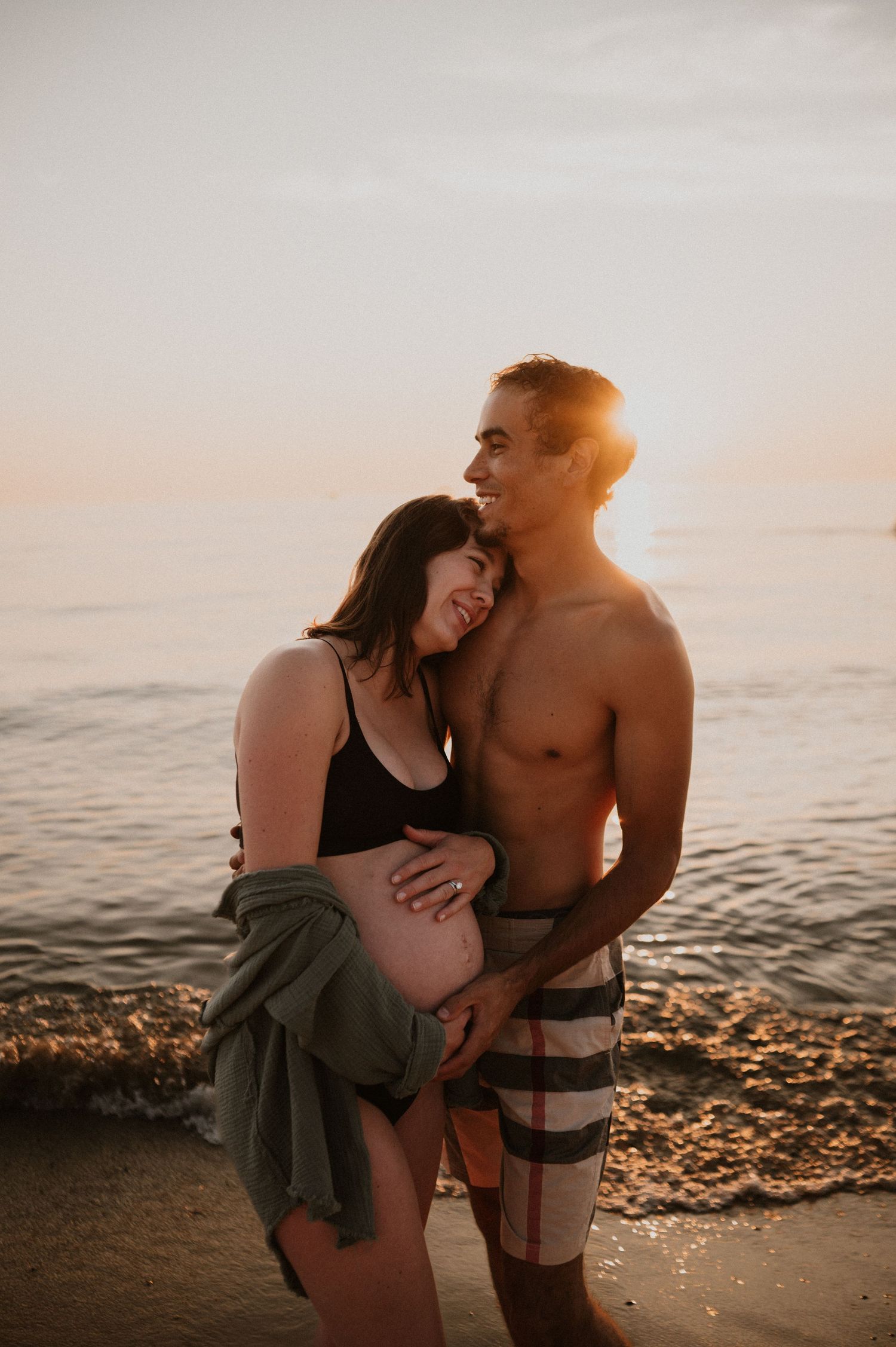 Joyful maternity beach photo with warm sunset lighting and waves in background.