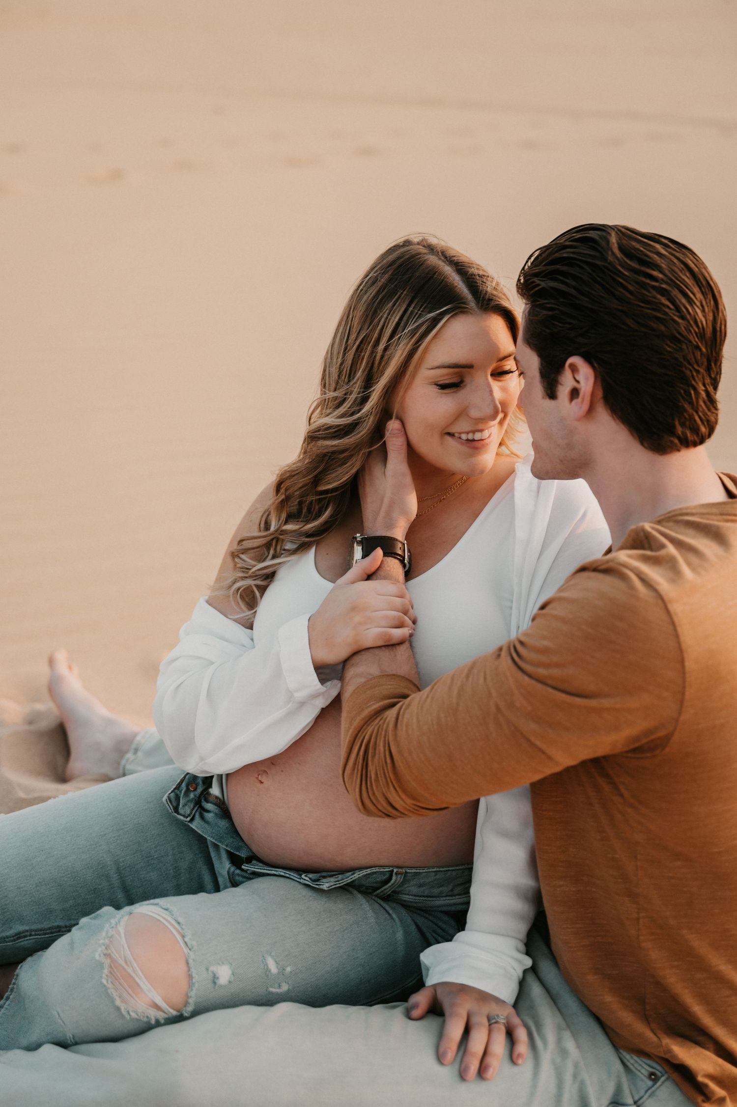 Intimate desert maternity session shows couple sharing tender moment on sand dunes.