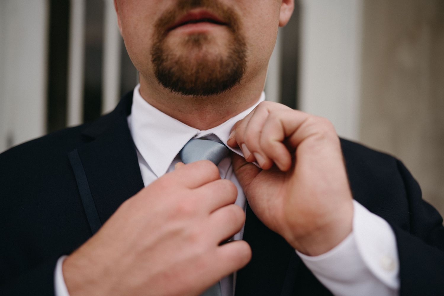 Close-up detail shot of groom adjusting his tie before the ceremony.