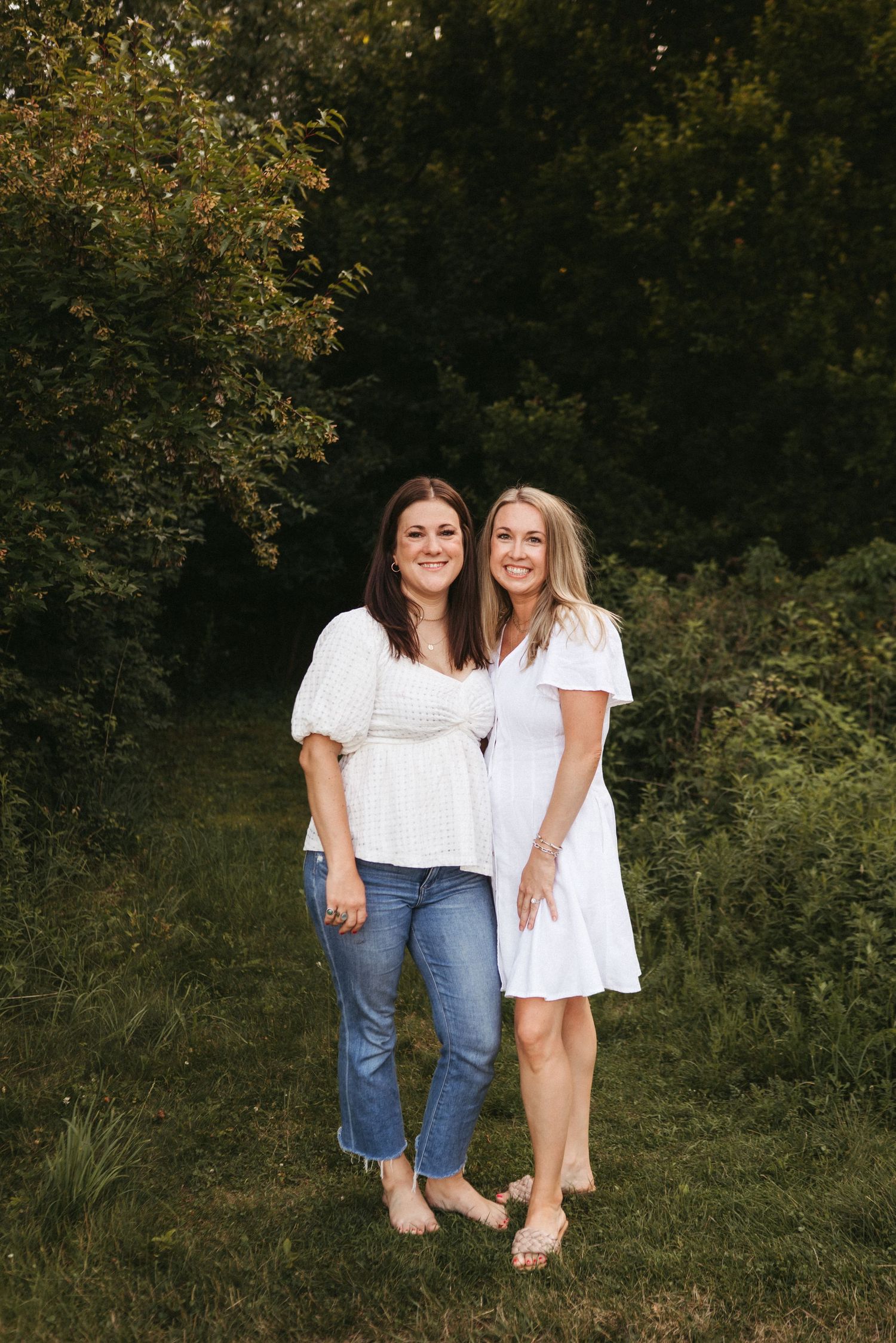 Two friends in casual white tops and denim share a candid moment outdoors.