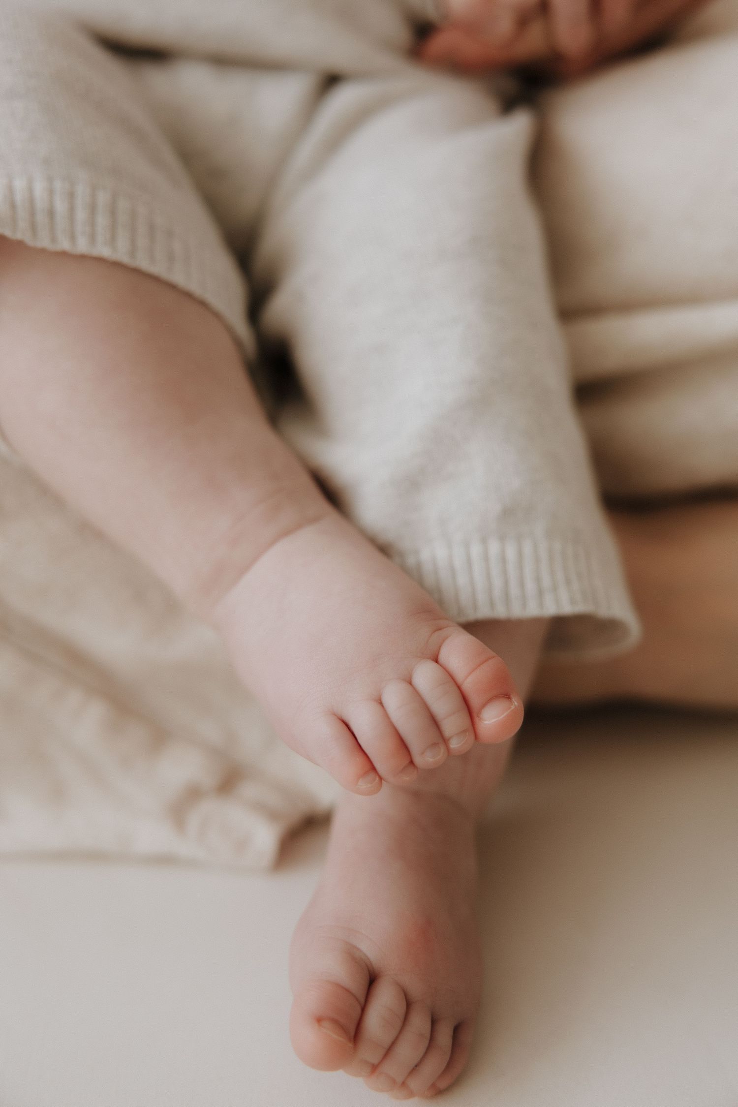 Close-up of tiny newborn baby feet in a soft beige knit outfit.
