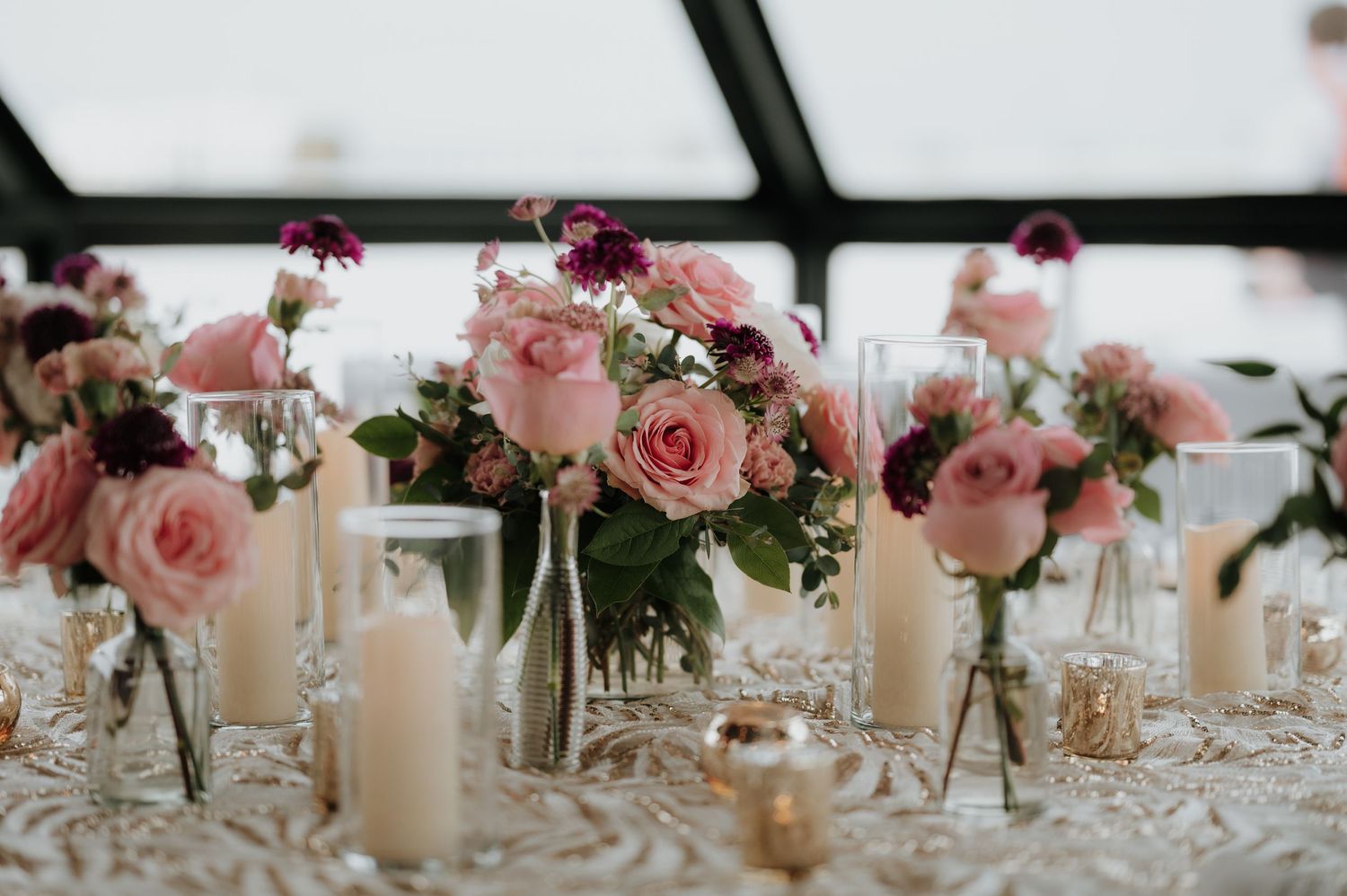 Pink rose centerpieces and white candles line reception tables creating romantic ambiance.