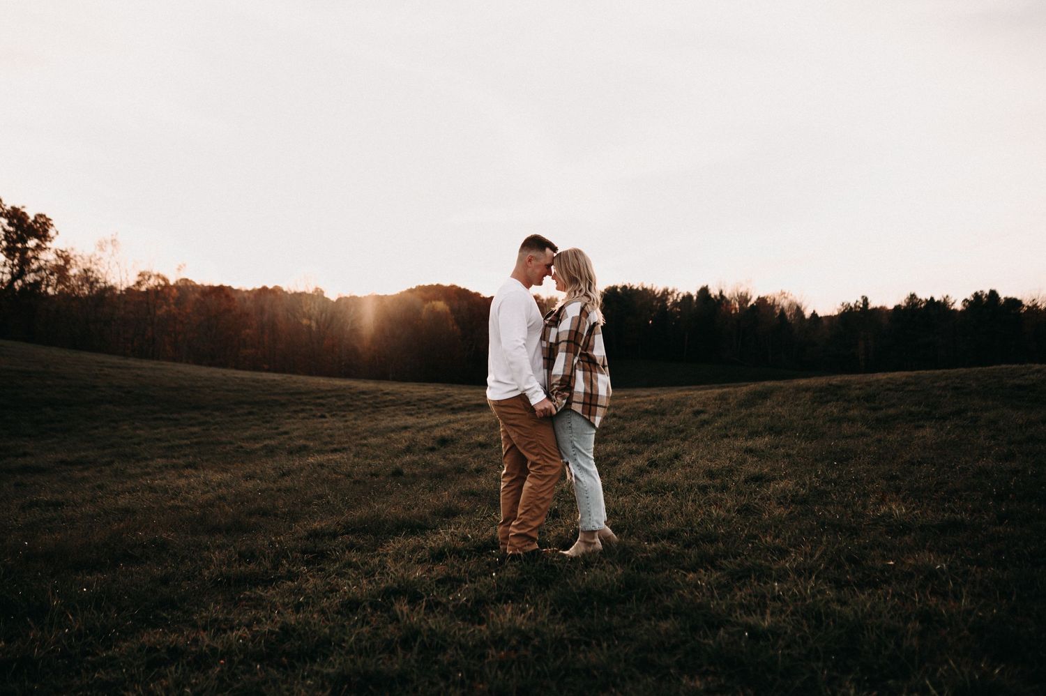 Couple embracing in golden sunset light on grassy hillside.