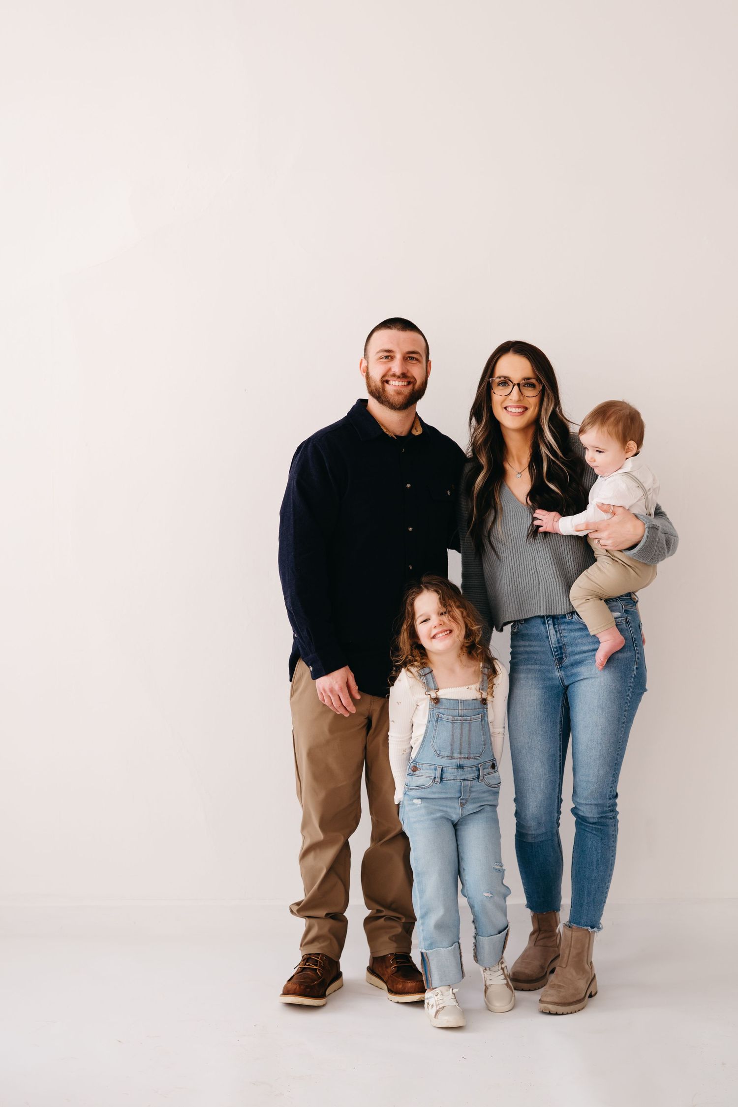 Family of four standing together against plain white backdrop in studio setting.