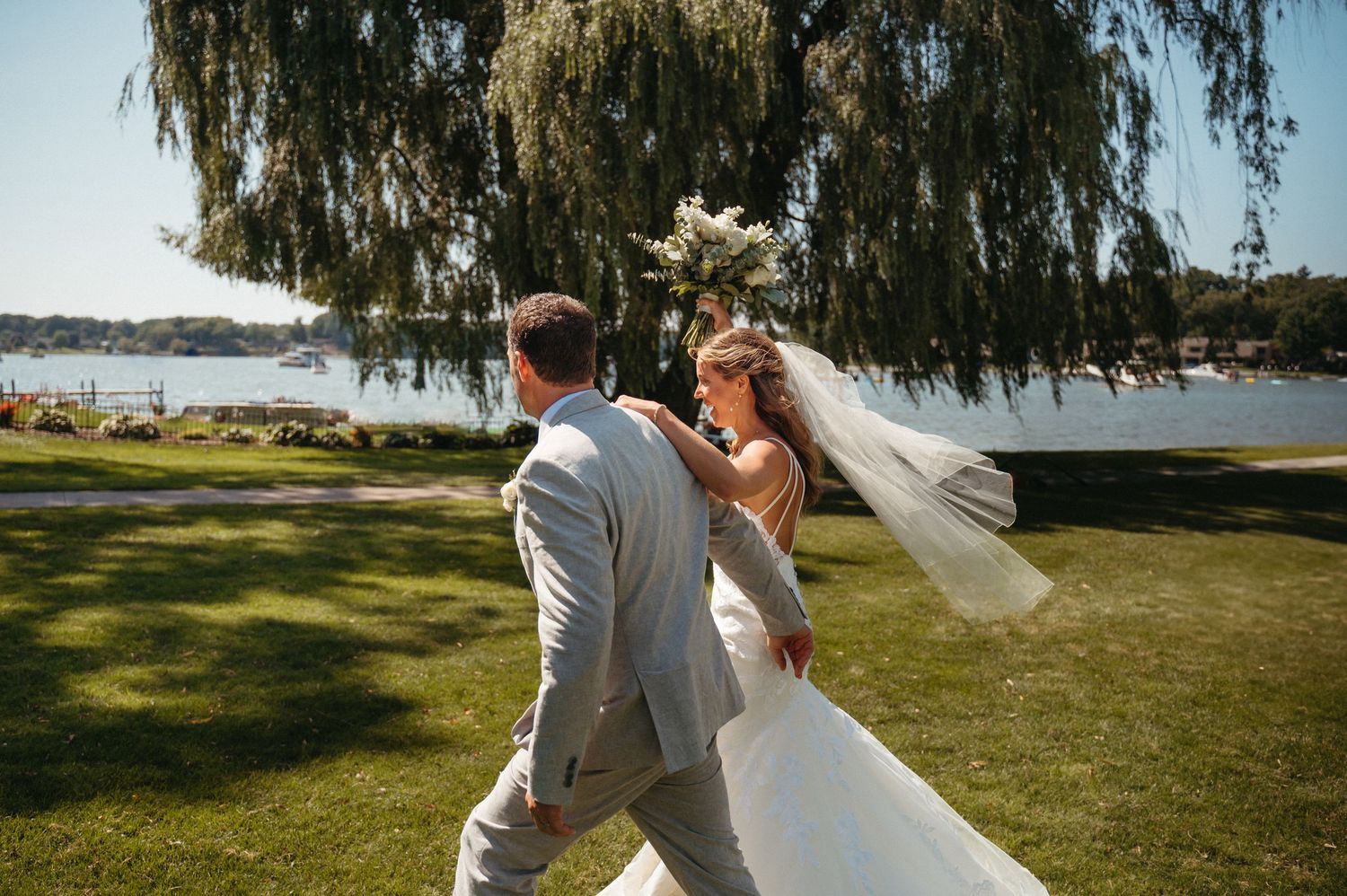 Wedding celebration on a scenic waterfront lawn with willow trees in the background.