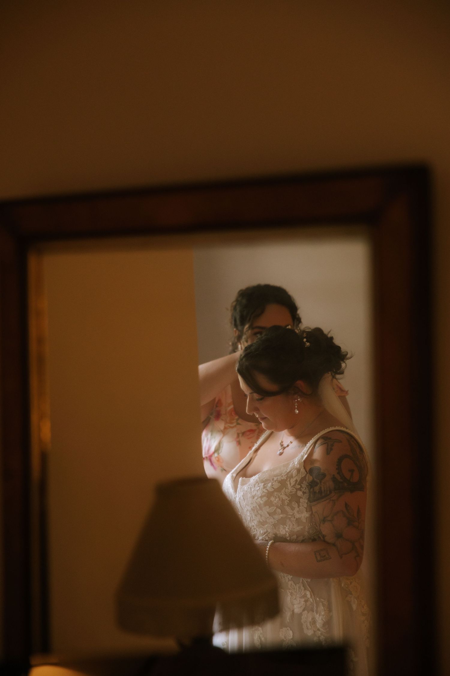 A series of warm-toned photographs showing a bride getting ready in a lace wedding dress in soft window light.