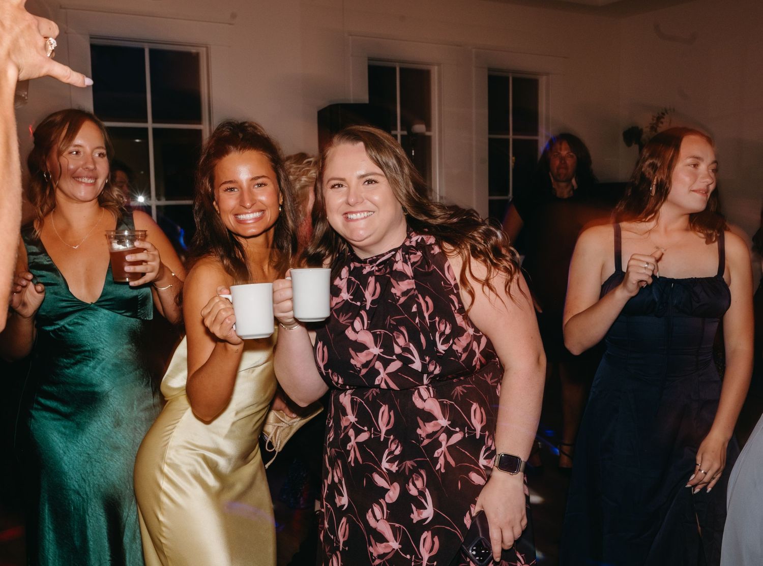 Wedding guests in formal dresses celebrate at a reception with drinks and laughter.