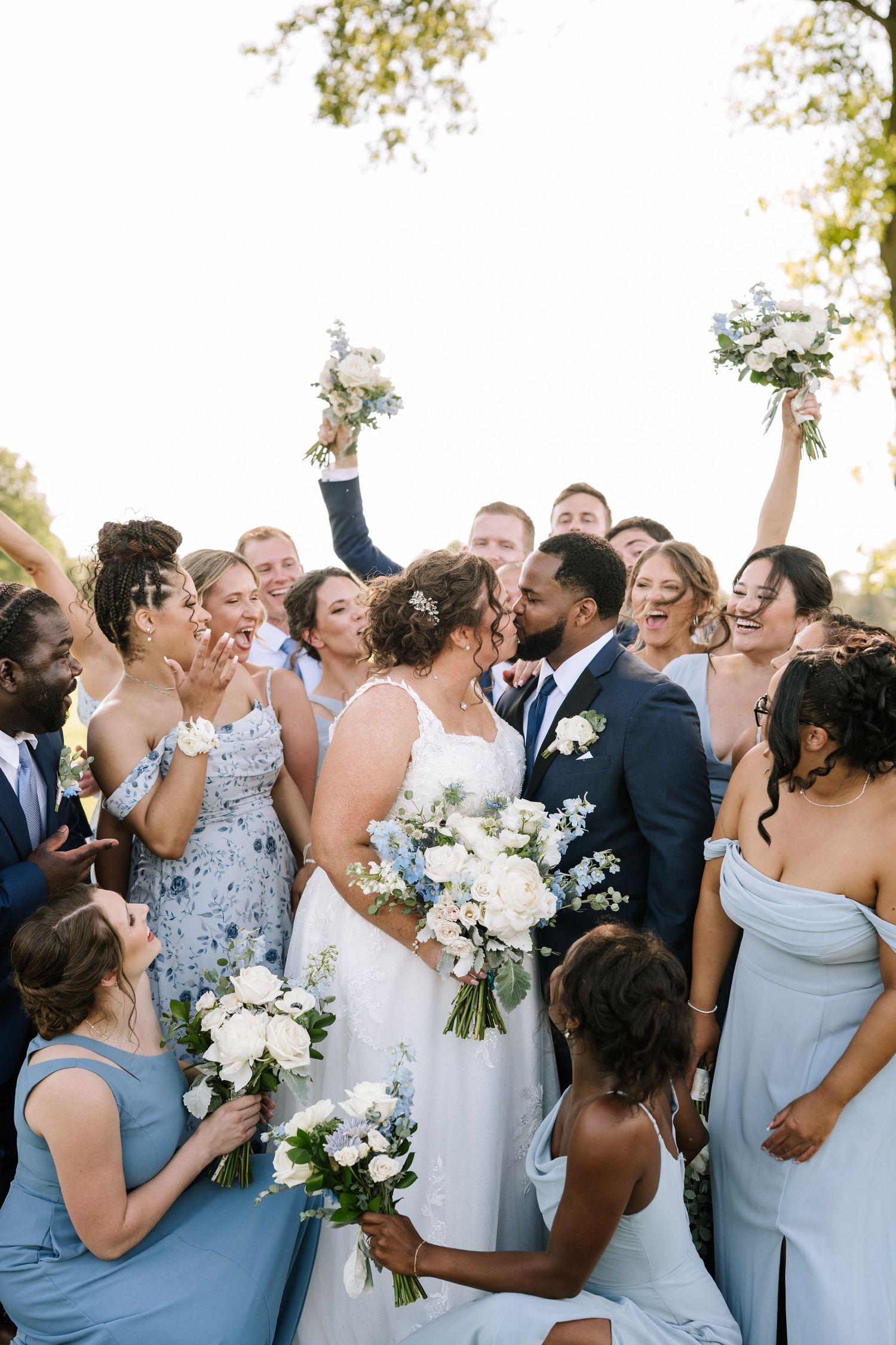 Wedding party in blue and white attire celebrating joyfully outdoors.