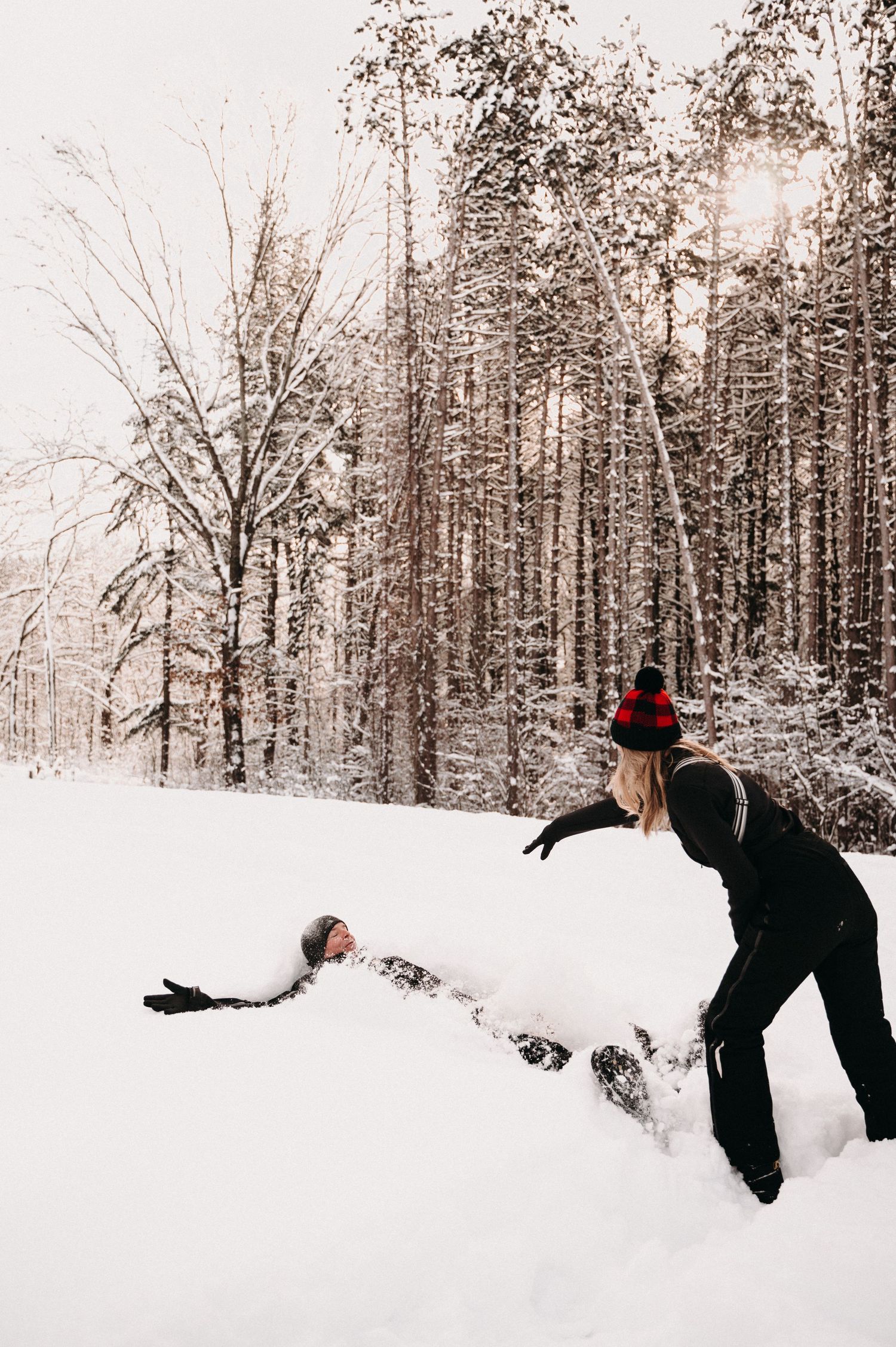 Playful winter scene of two people having fun in deep snow surrounded by trees.