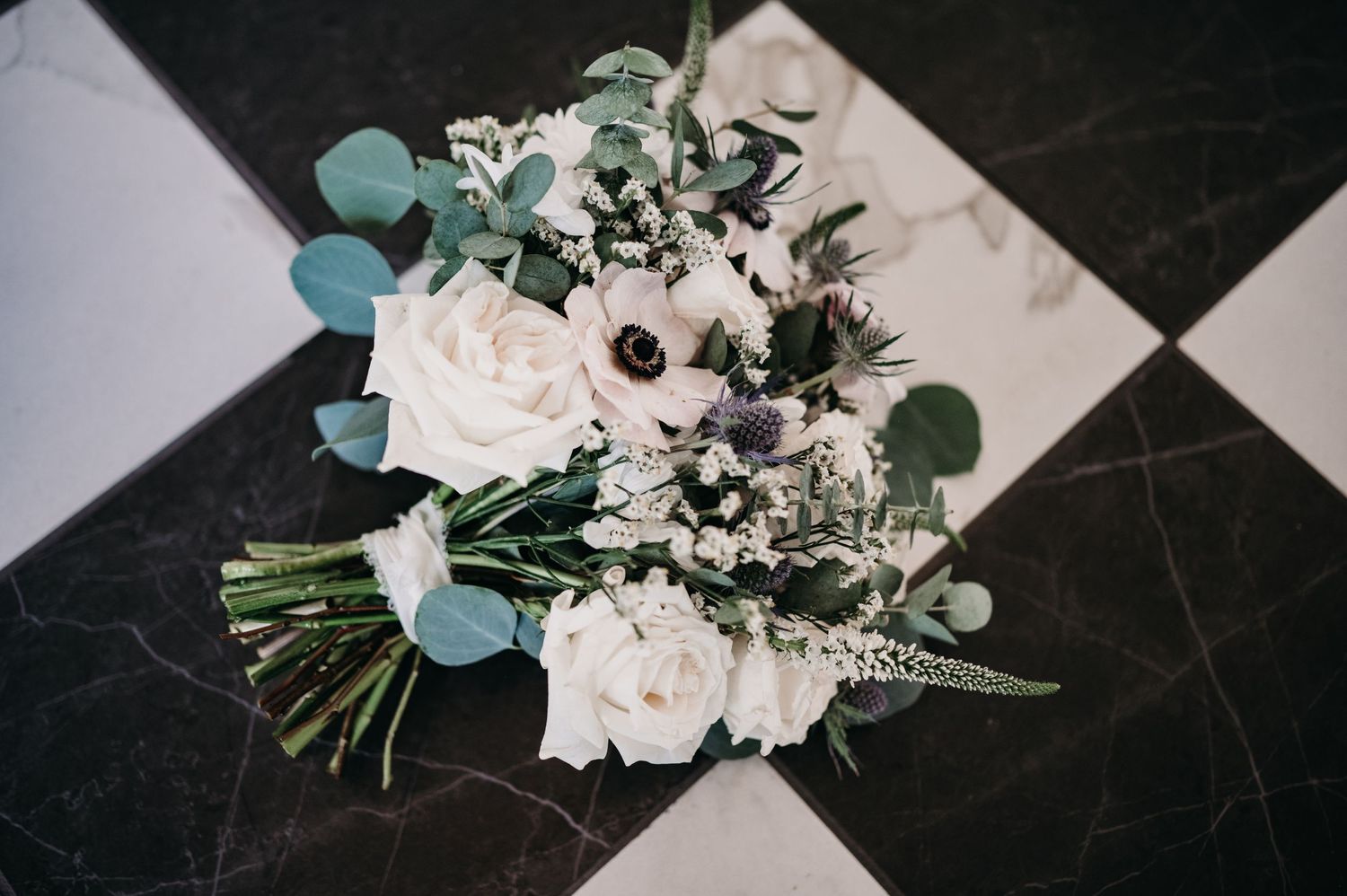 Wedding floral arrangement with white roses and anemones against a black and white checkered floor.