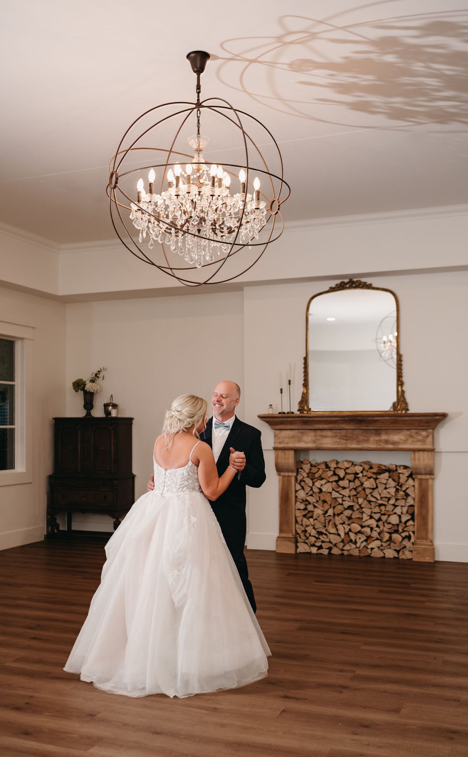 Elegant ballroom with hardwood floors, ornate chandelier, and fireplace filled with decorative logs.