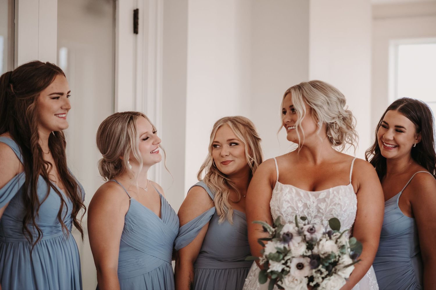 A bridal party in coordinated dusty blue dresses share a joyful moment together.